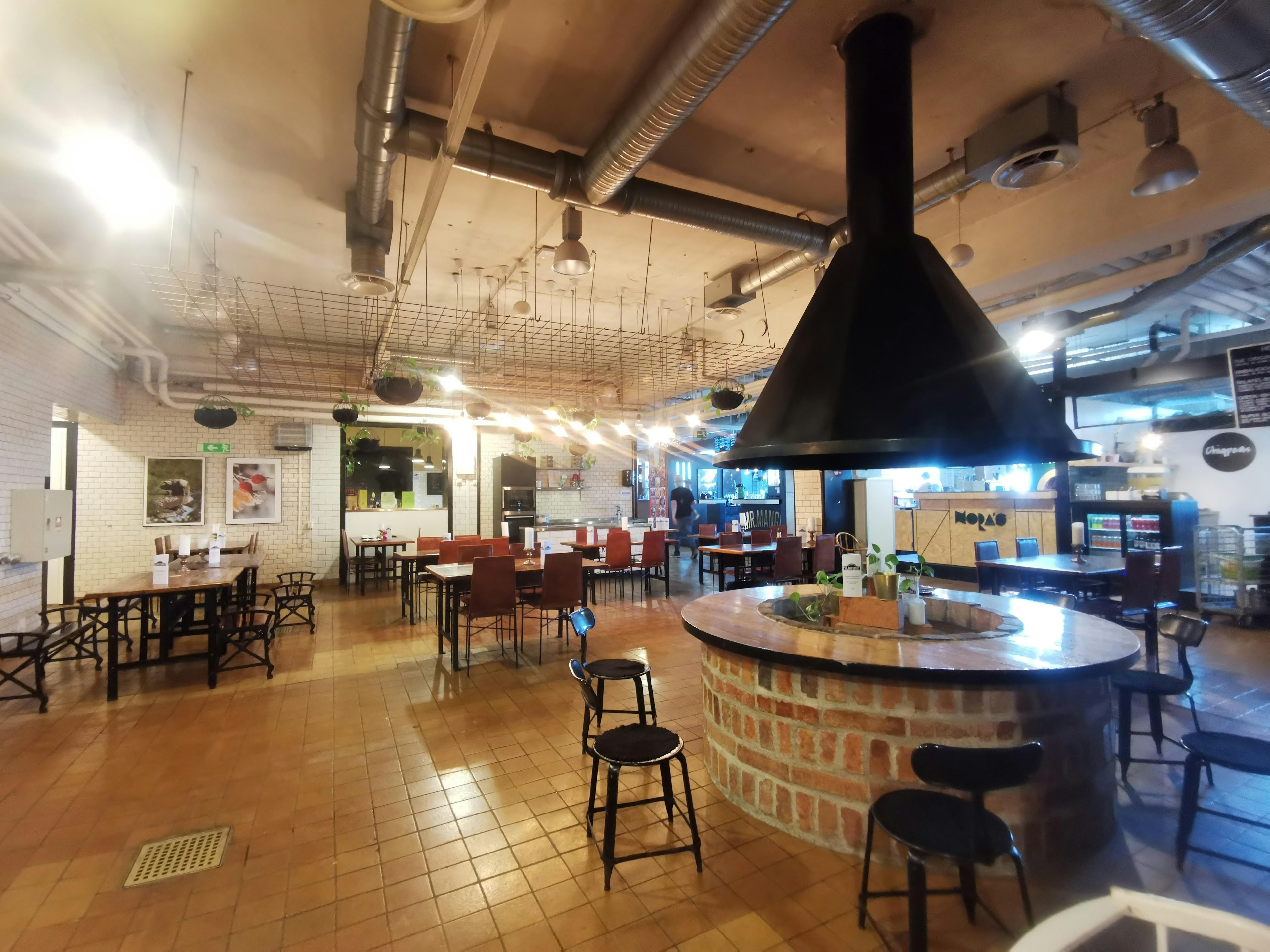 Intérieur spacieux d'un café avec un comptoir rond et une hotte noire, tables et chaises disposées