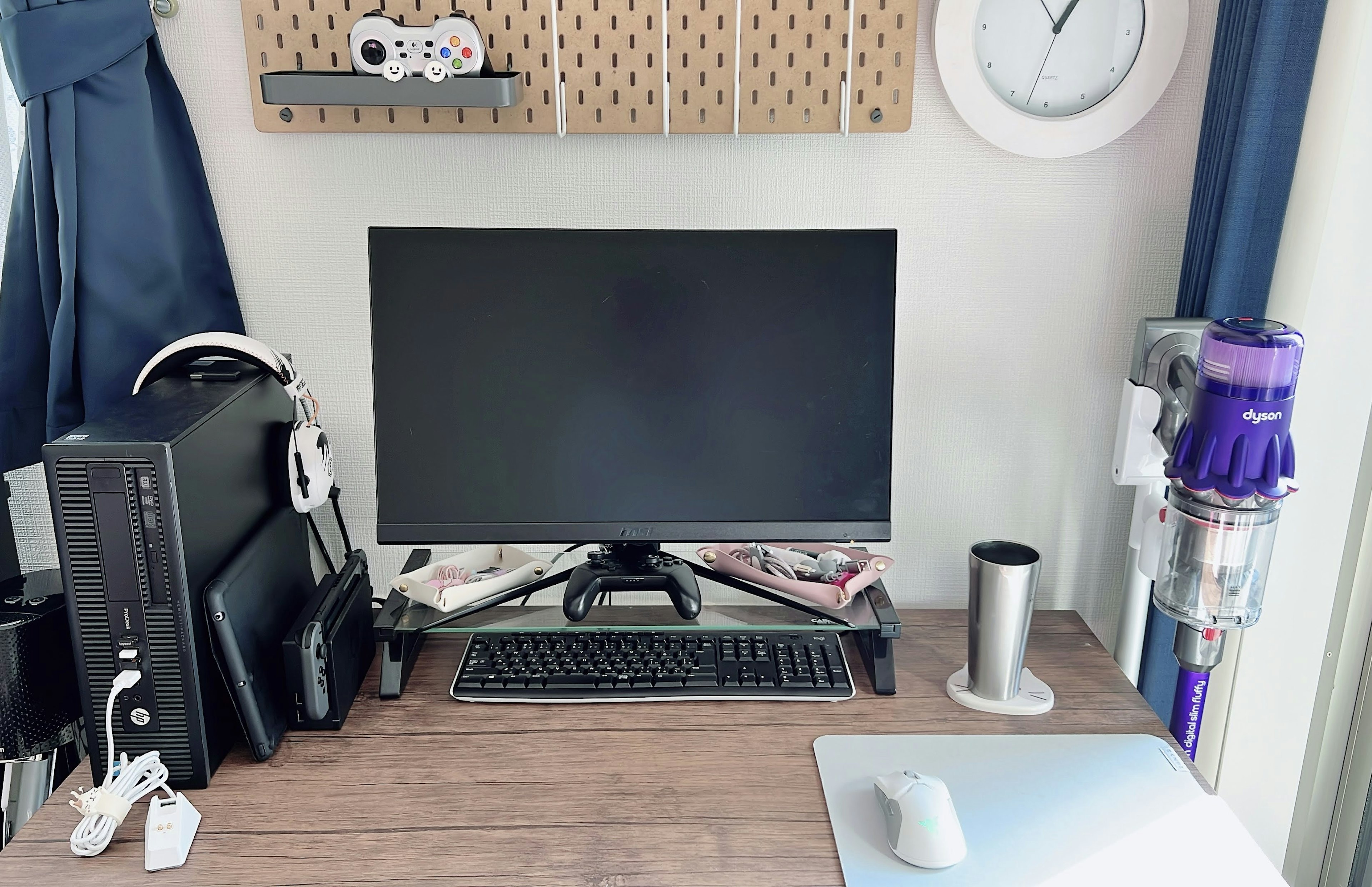 Workspace featuring a black monitor and keyboard with a vacuum and cup by the window