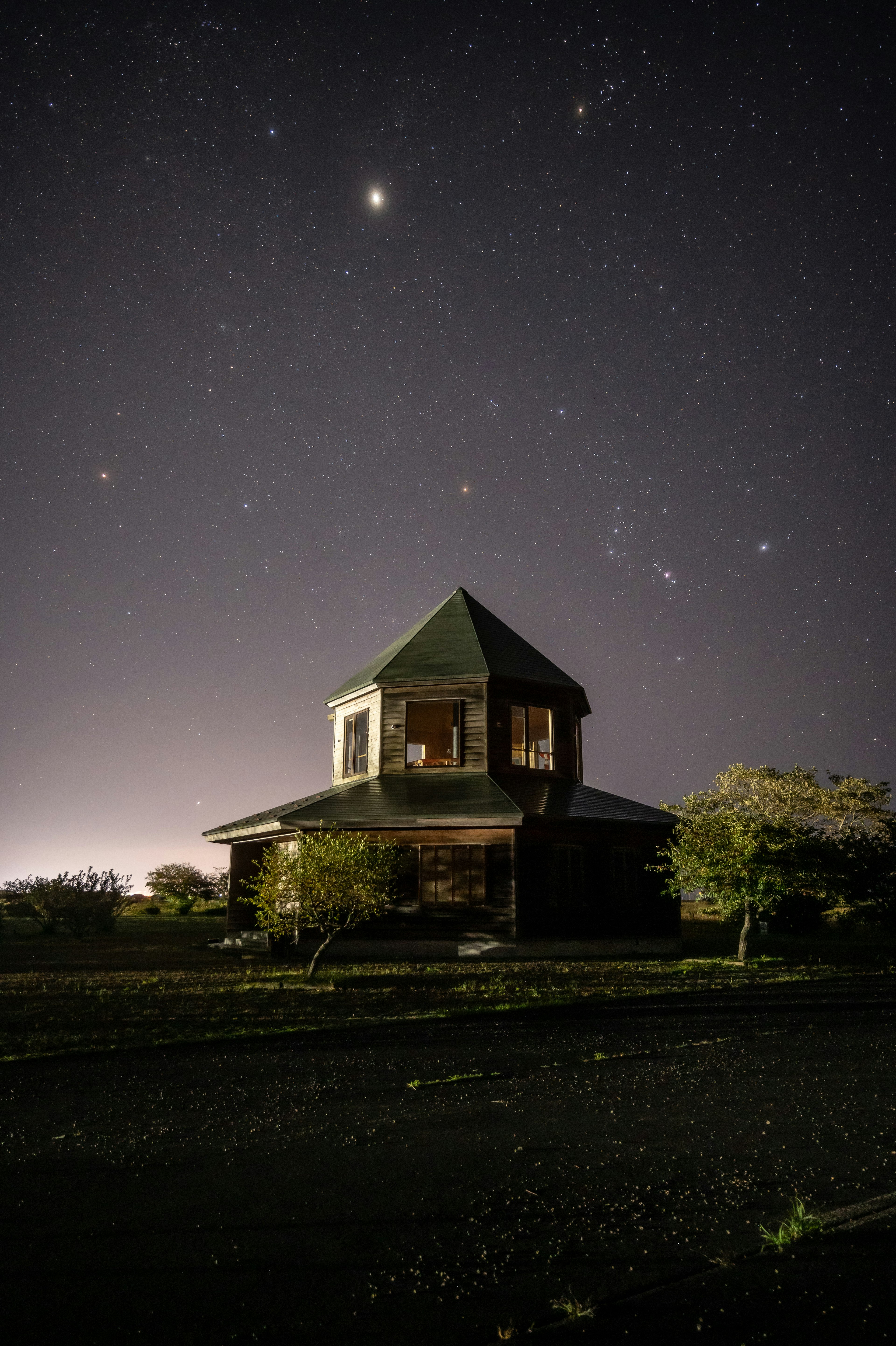 夜空の星々の下に立つ古い三角屋根の家と周囲の木々