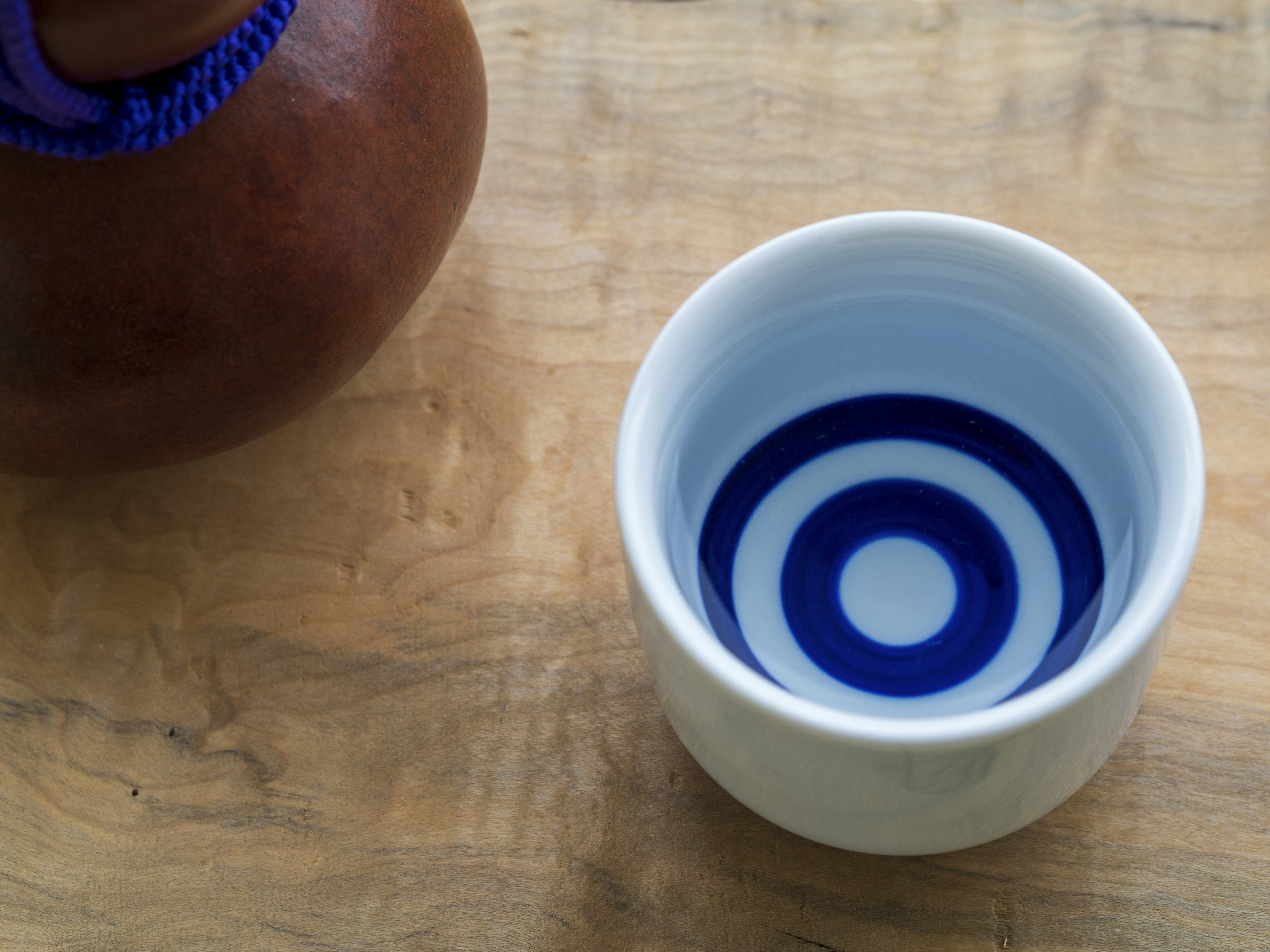 A white ceramic bowl with blue concentric circle pattern next to a brown pot