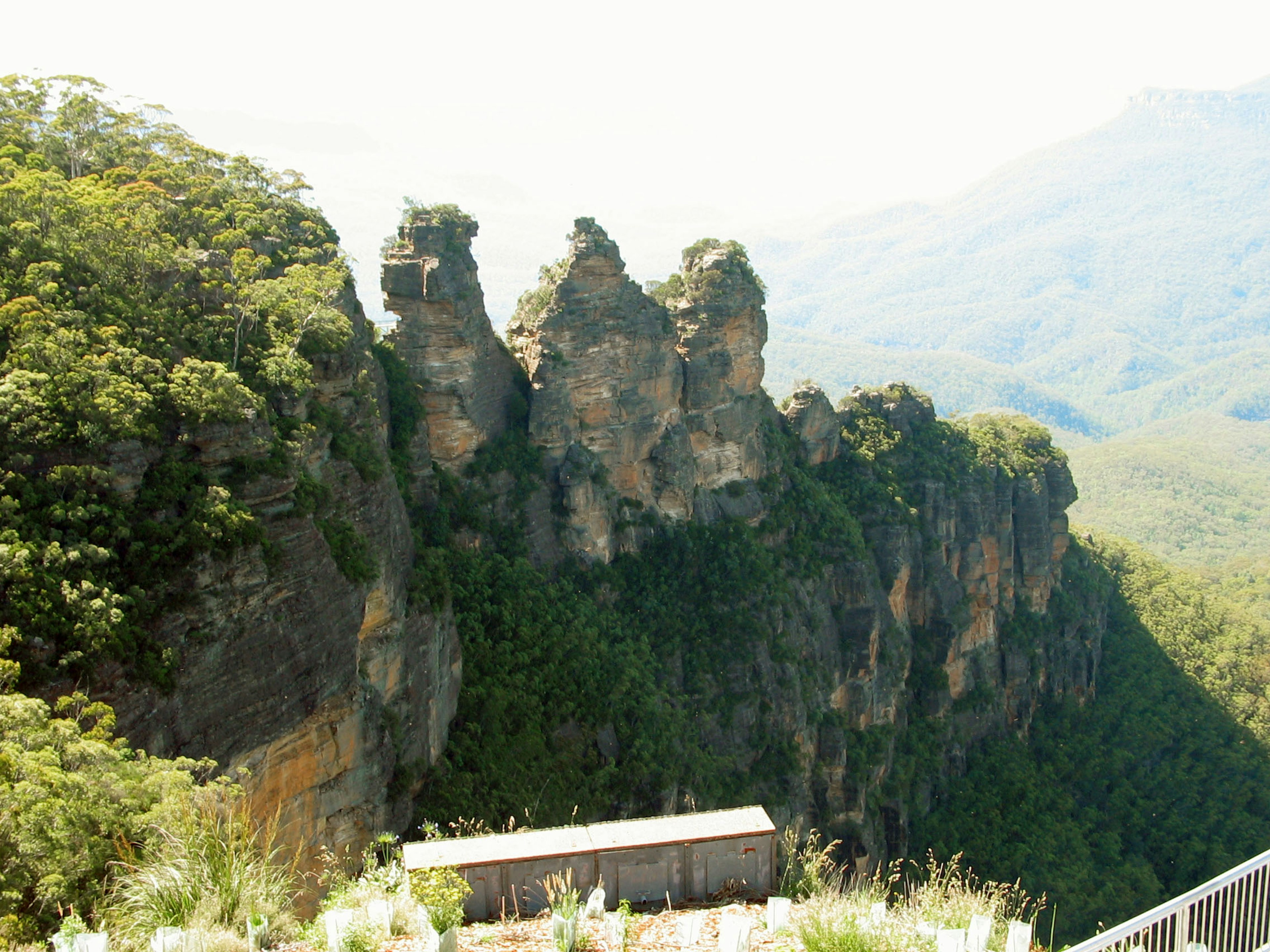 Paisaje natural con tres picos rocosos contra montañas azules