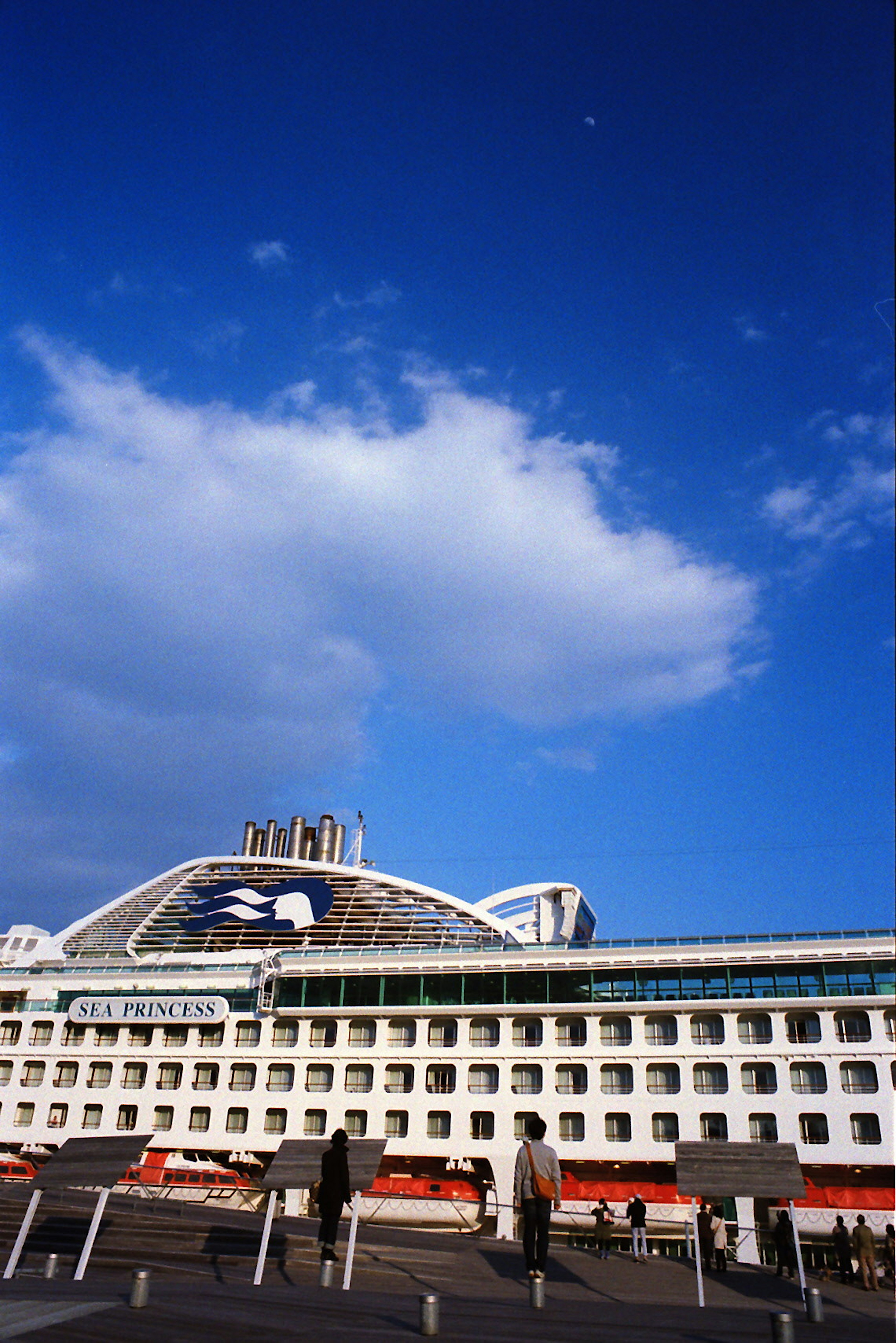 Modern building exterior under blue sky with clouds and people