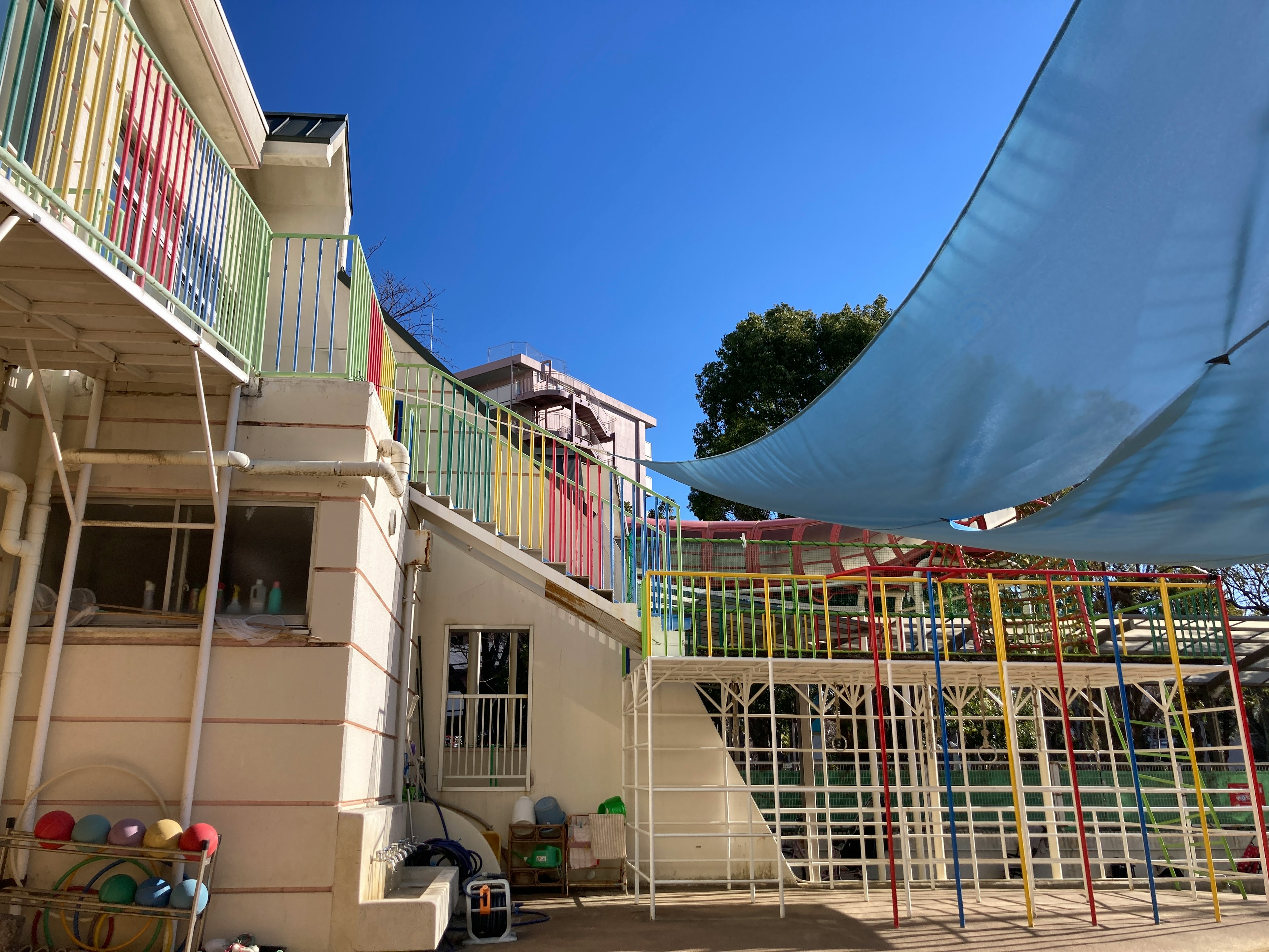 Spielplatzbereich eines Kindergartens mit bunten Strukturen und einem blauen Schatten