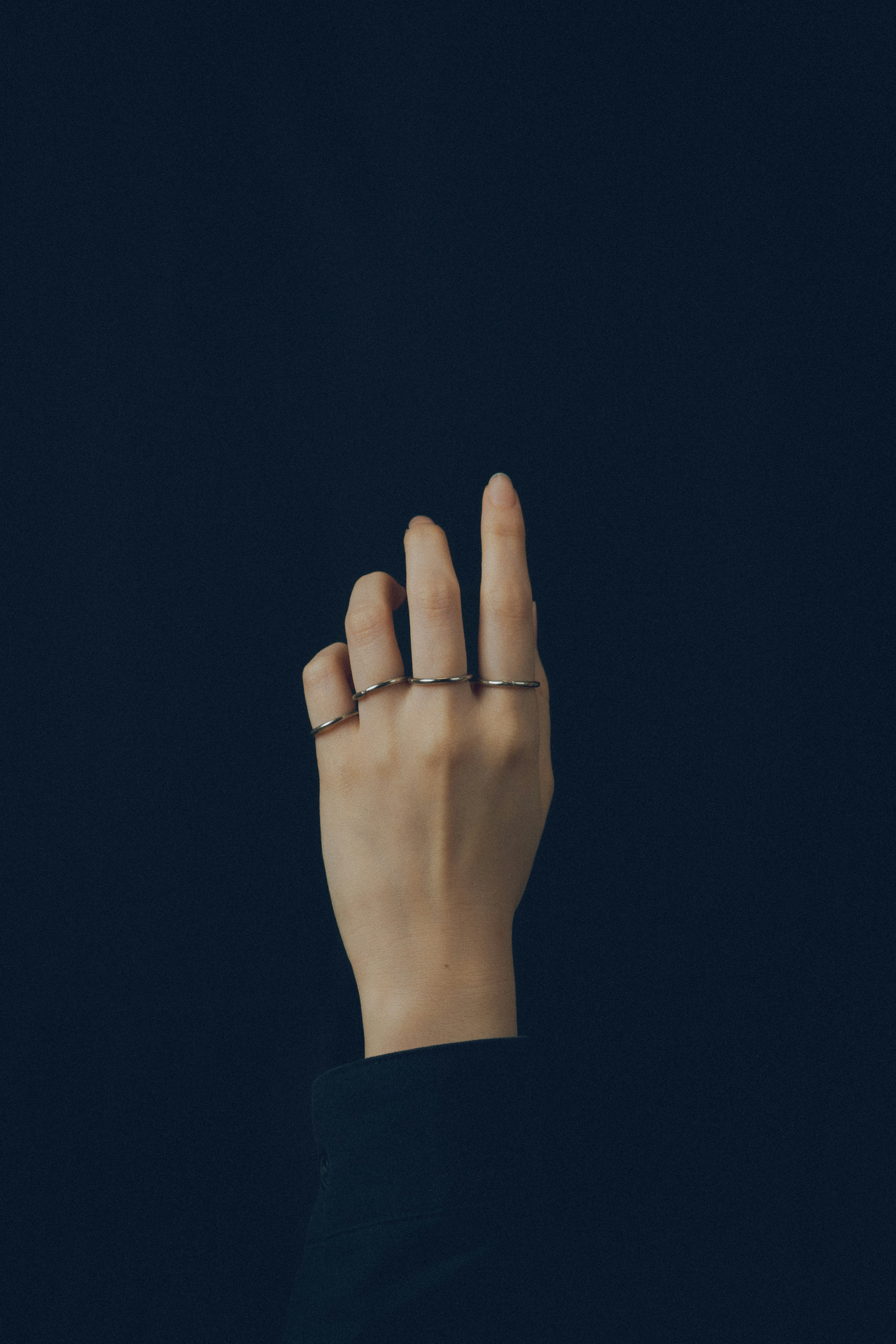 Una mano con anillos posicionada contra un fondo azul oscuro