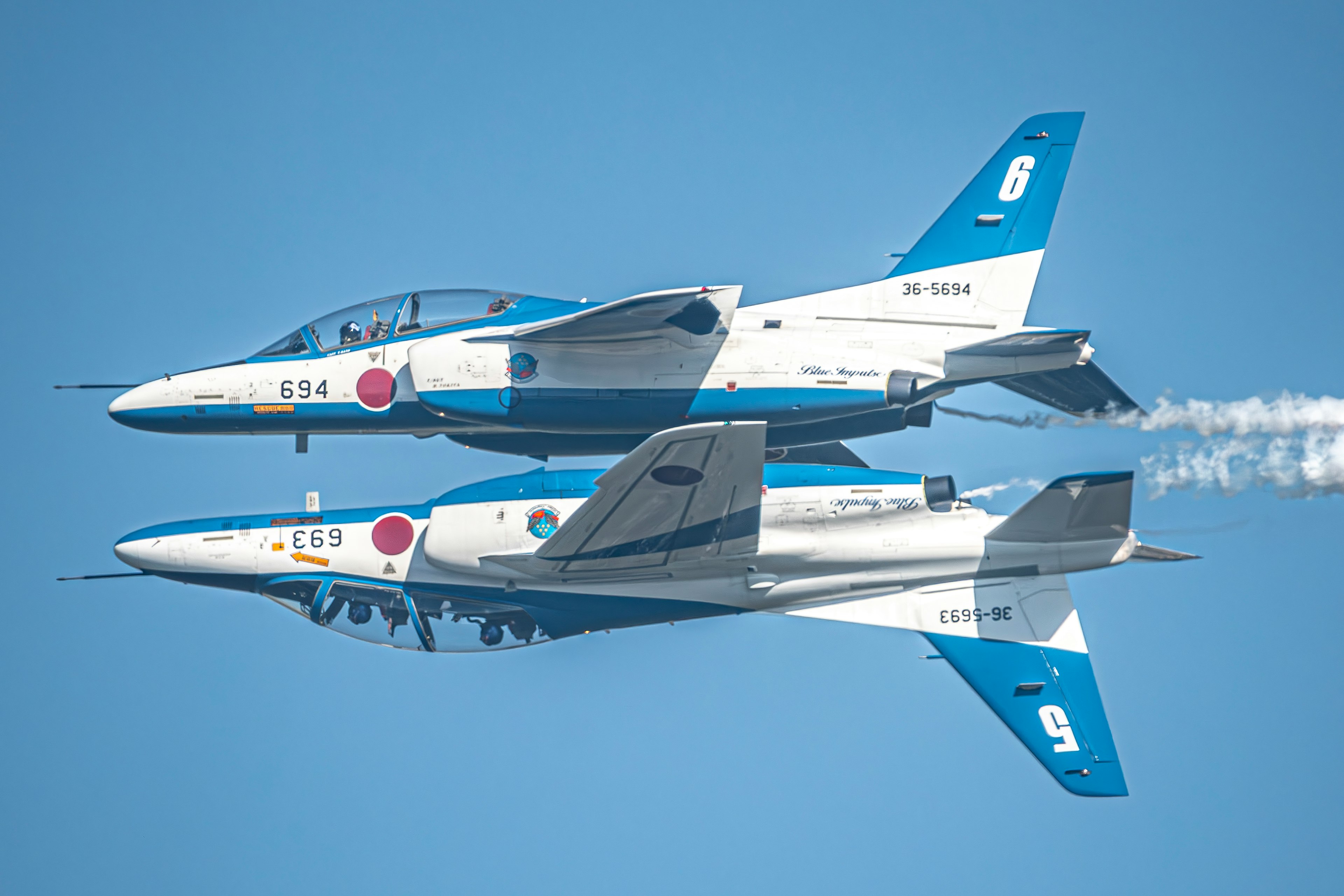 Zwei Flugzeuge fliegen in Formation vor einem klaren blauen Himmel