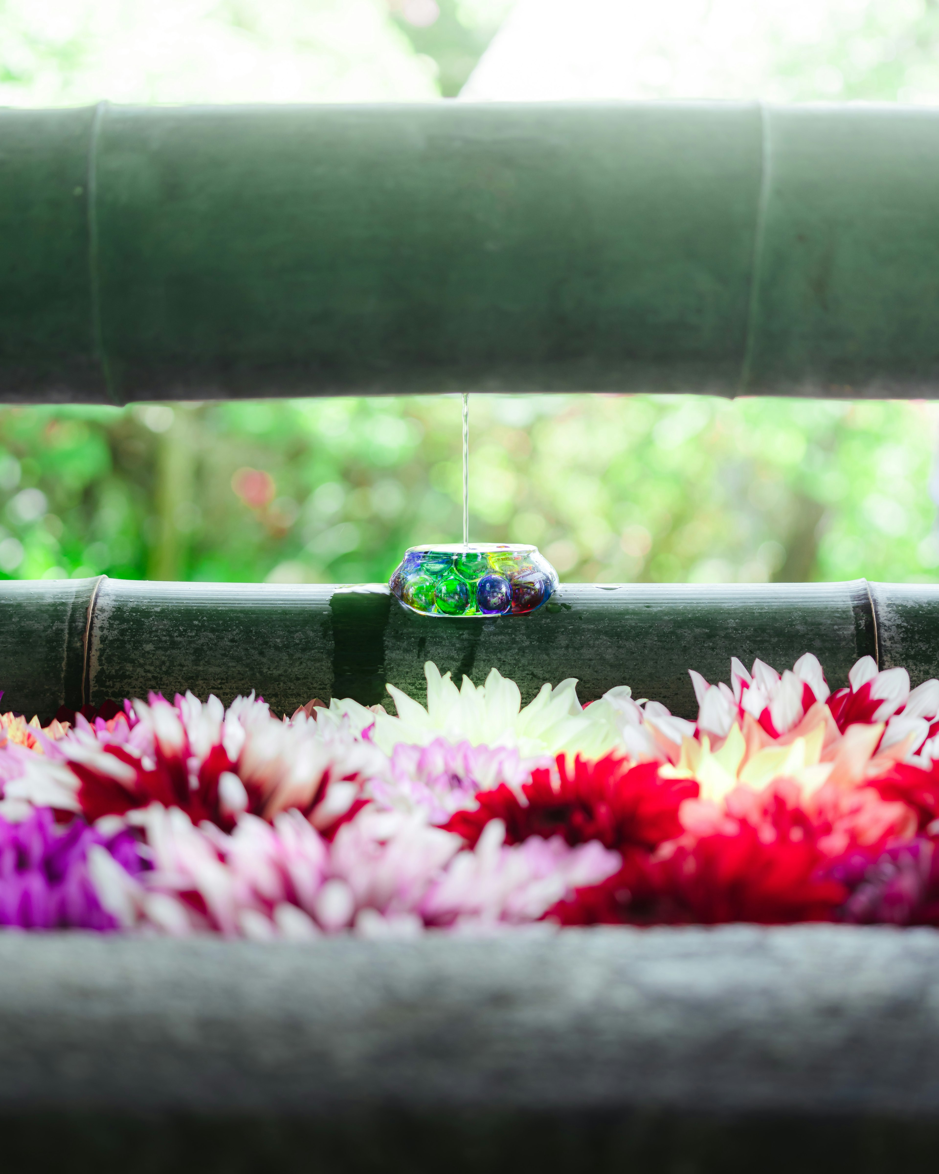 Colorful flowers arranged in front of a bamboo background with a decorative stone in green and blue