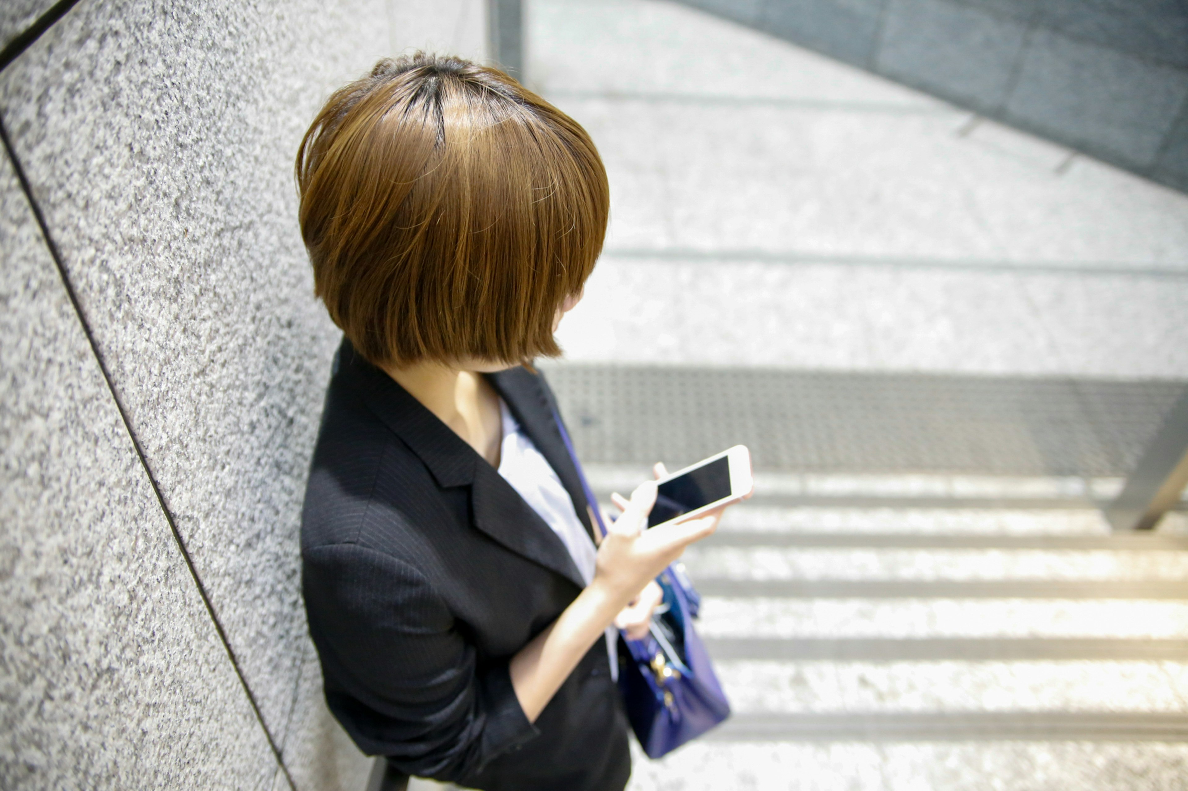 Una mujer de pie en las escaleras sosteniendo un teléfono inteligente Tiene un peinado corto y lleva un traje de negocios