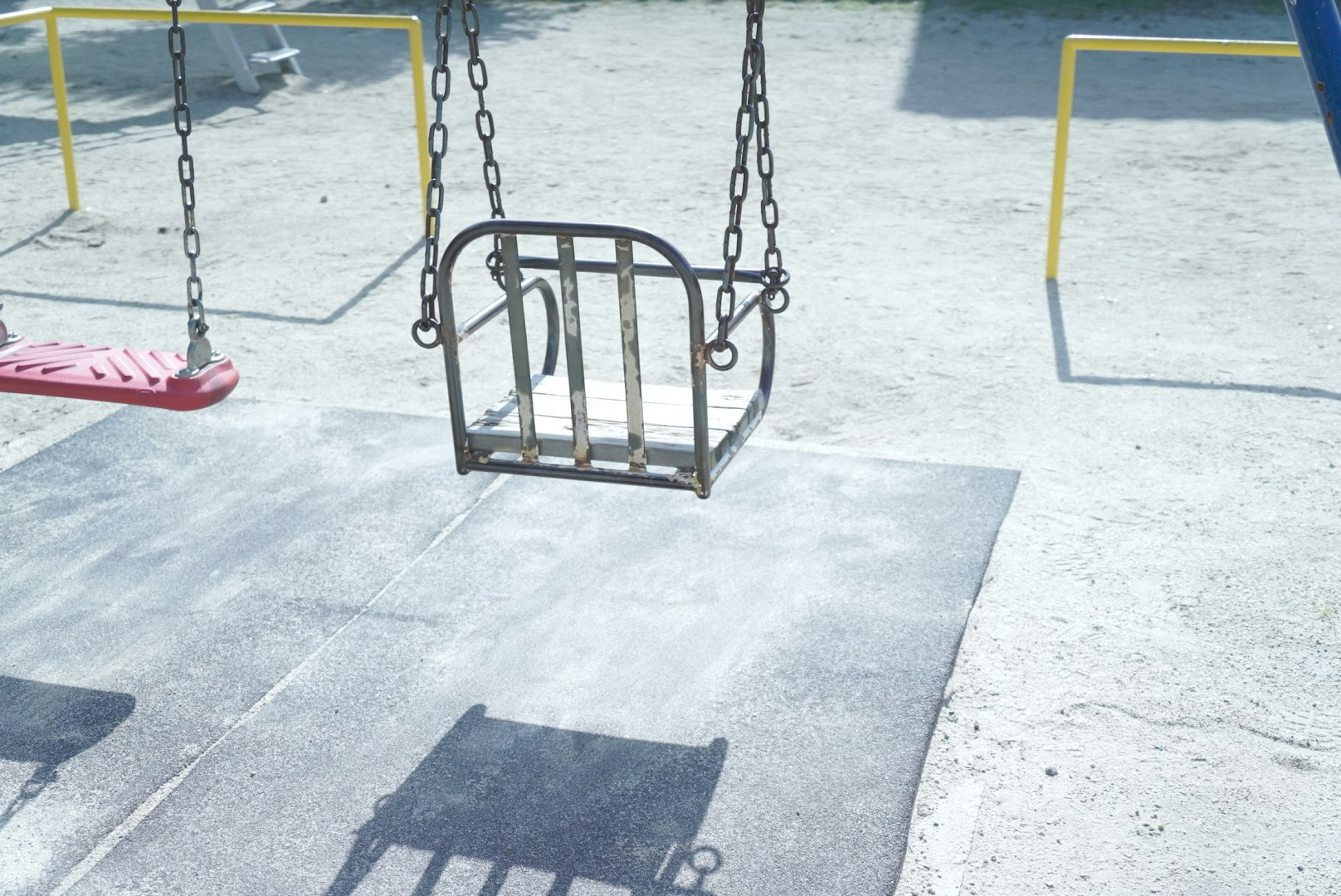 An empty swing hanging in a playground with a clear sky