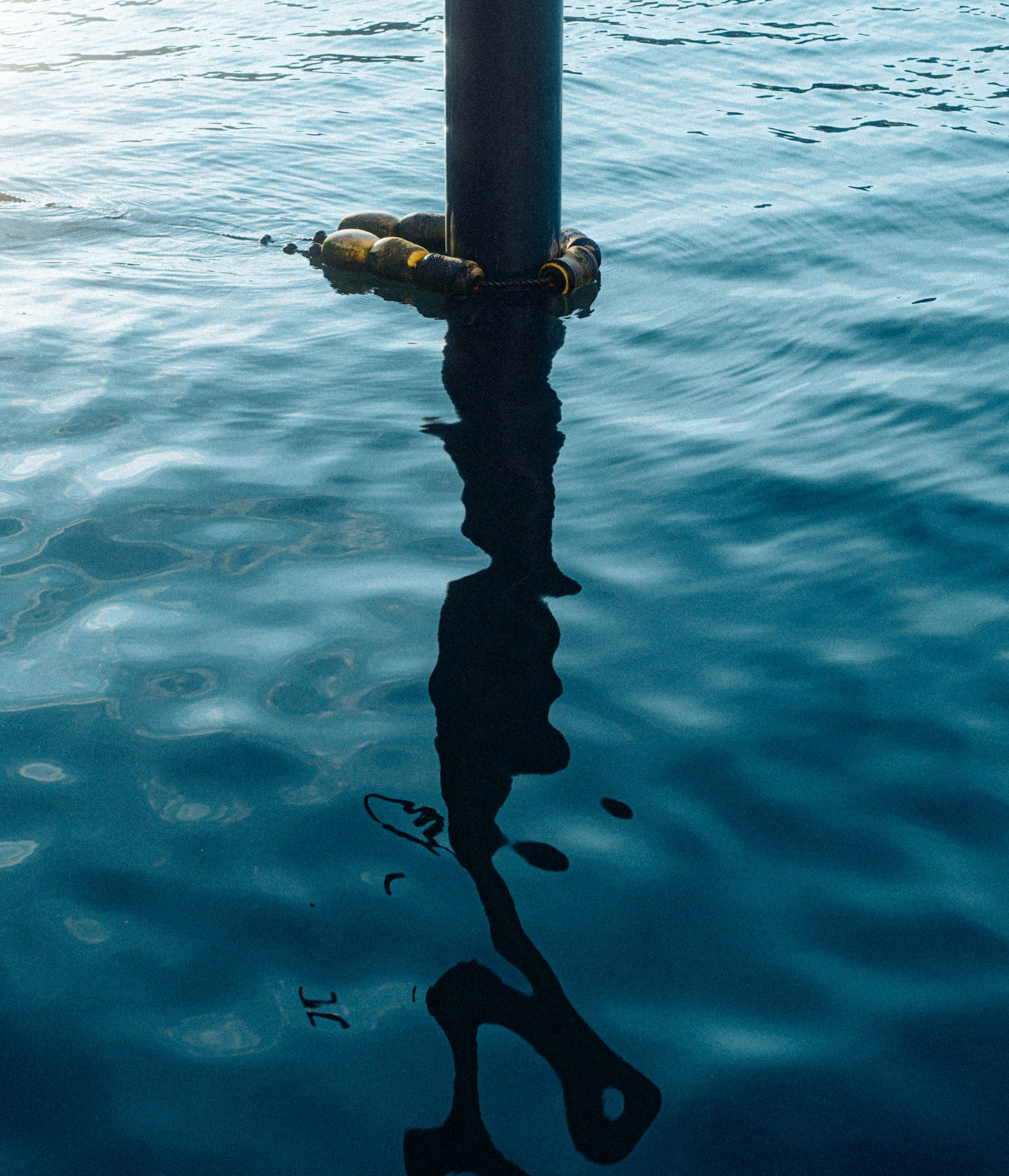 Reflejo de un poste en agua tranquila con una superficie azul clara