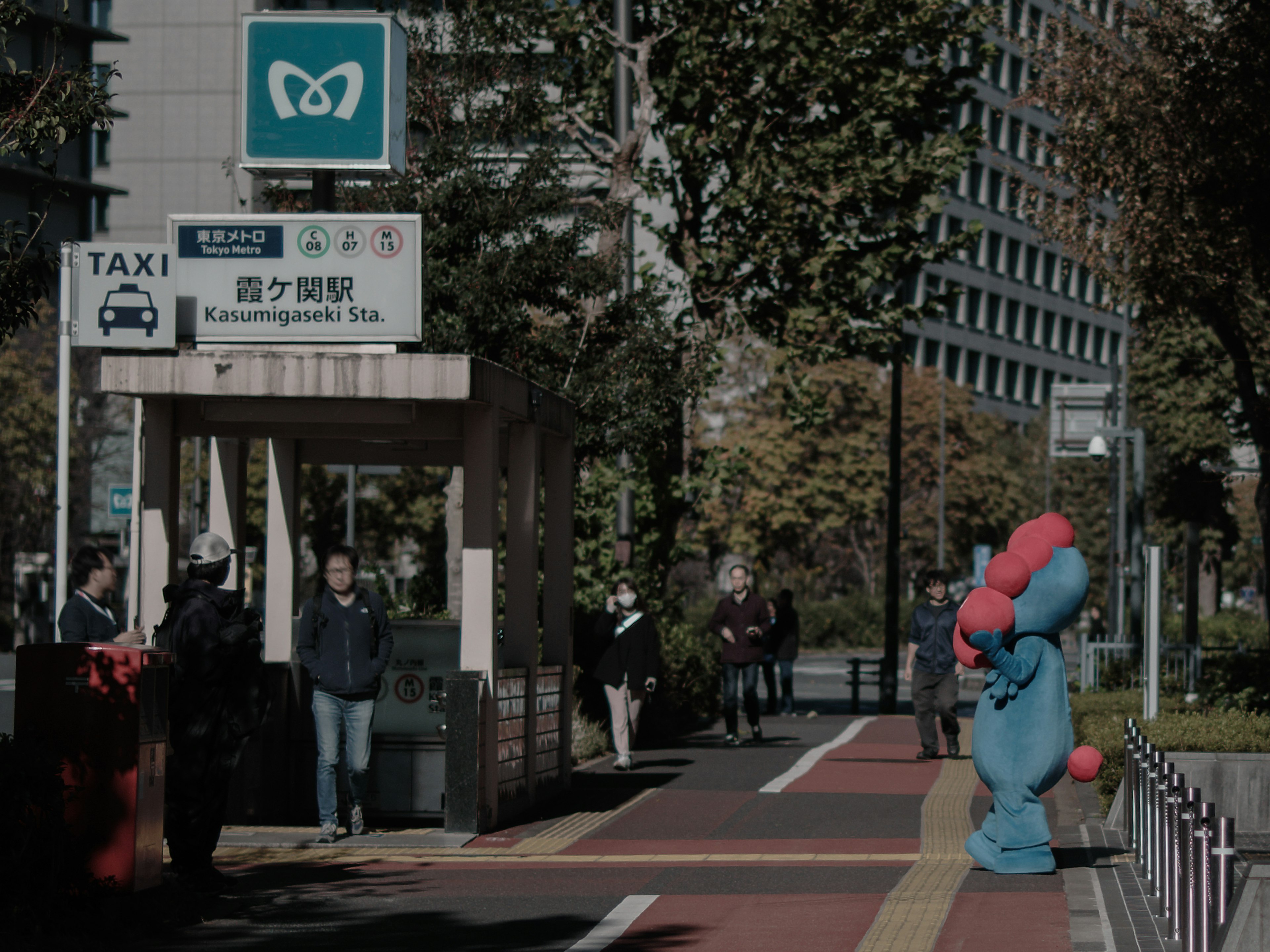 Personaggio mascotte blu in piedi a una fermata di taxi in un contesto urbano