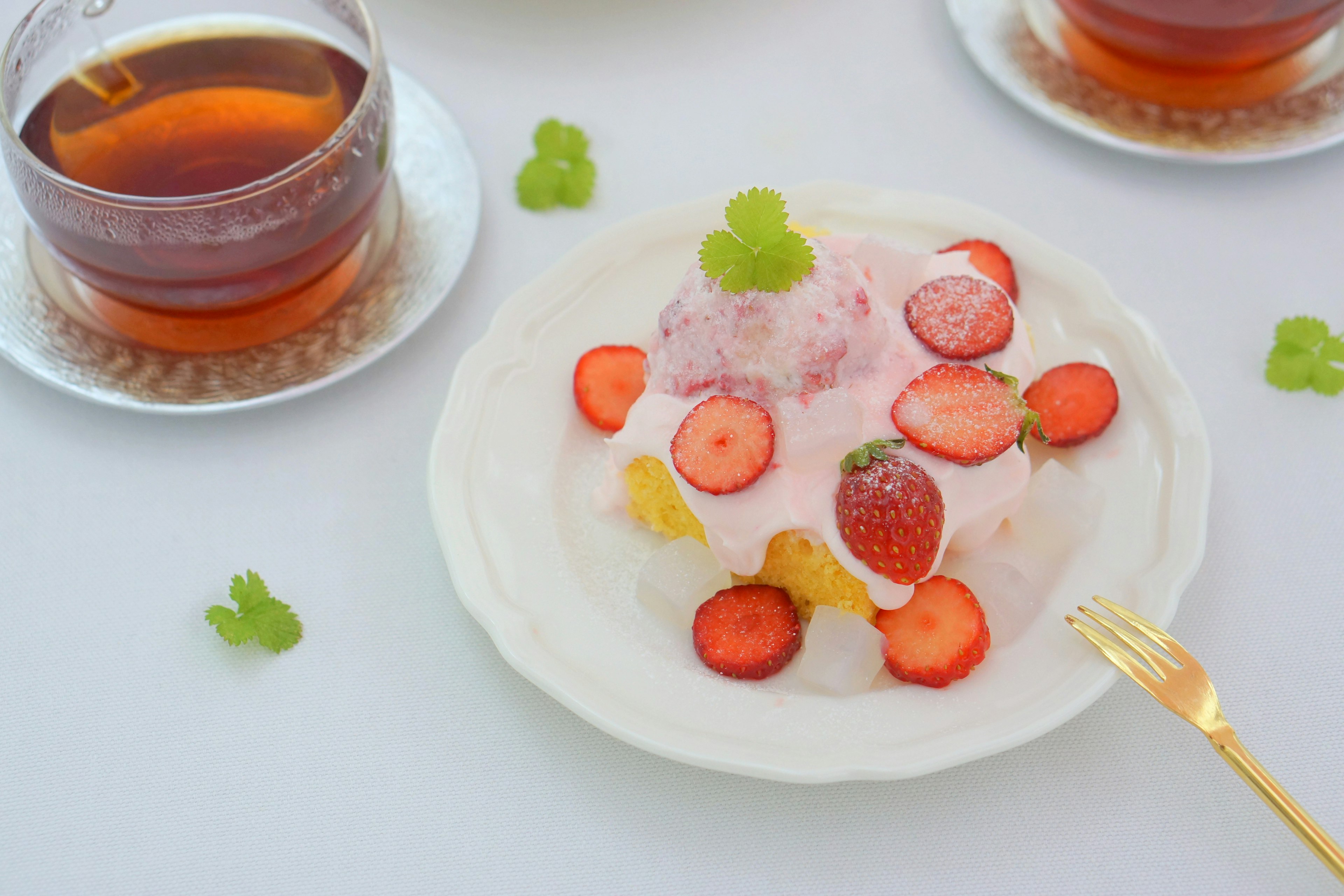 A dessert topped with strawberries and cream served on a plate with two cups of tea beside it