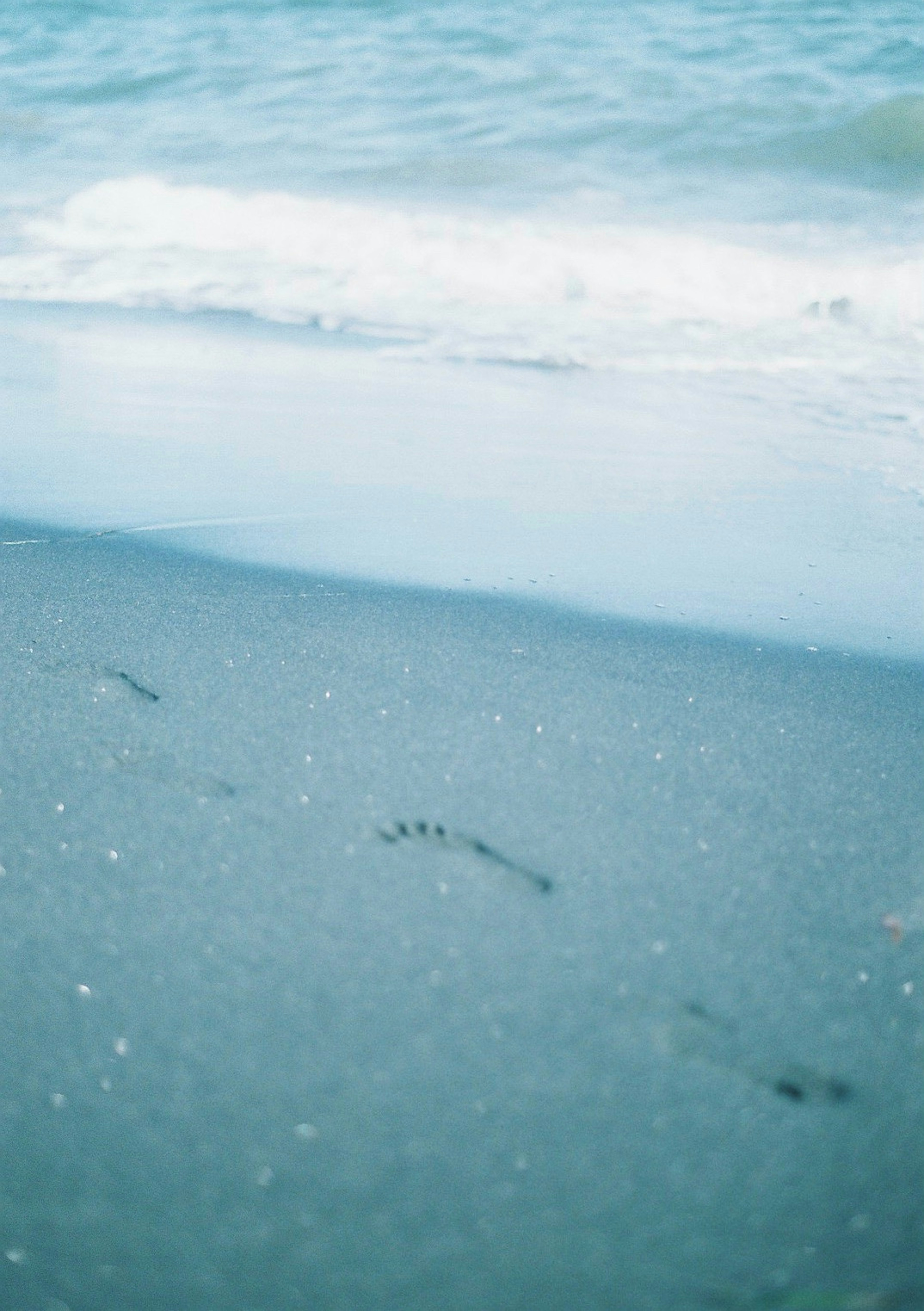 青い海と波のある砂浜に残る足跡