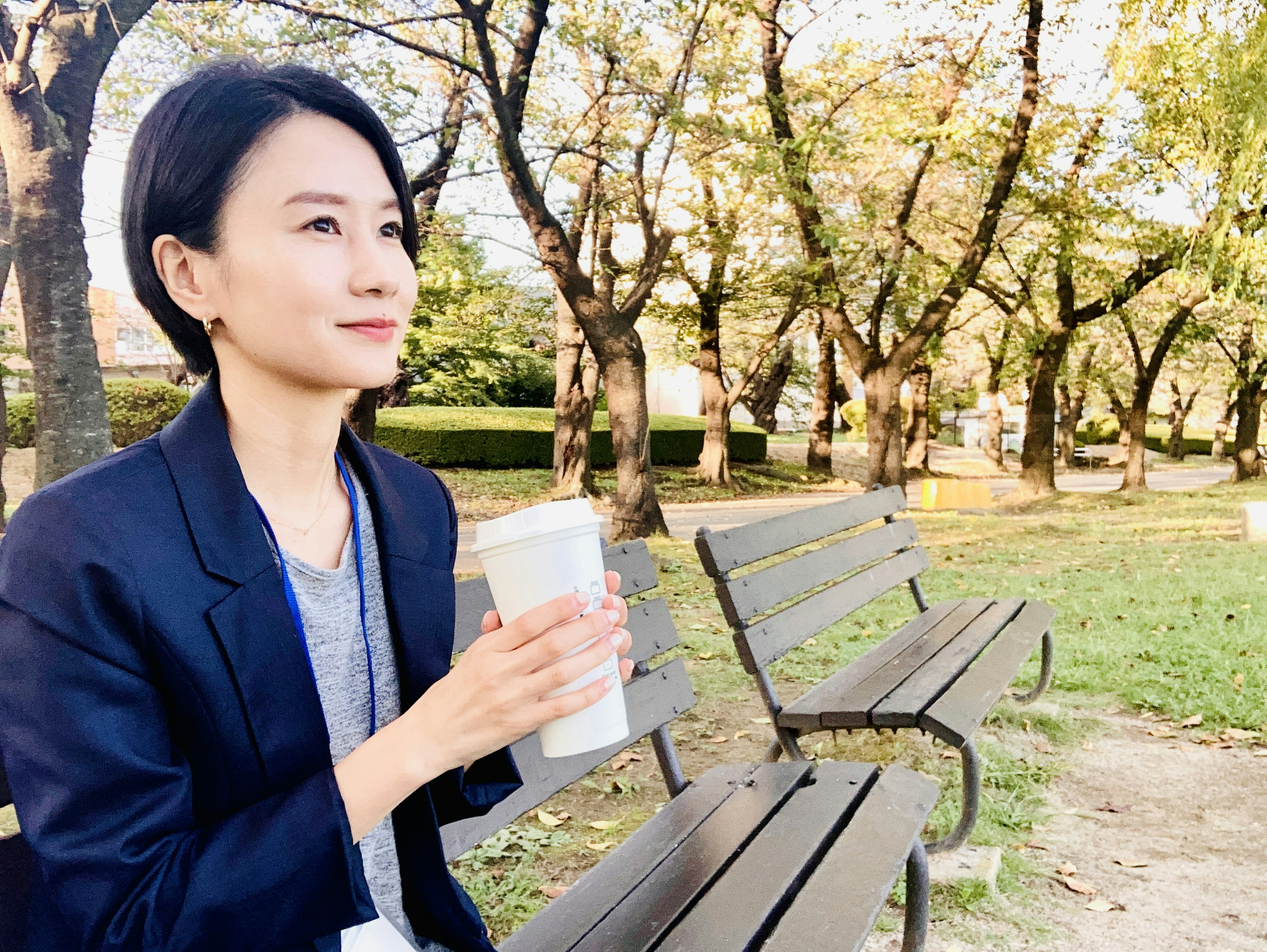 Mujer sentada en un banco del parque sosteniendo una taza de café