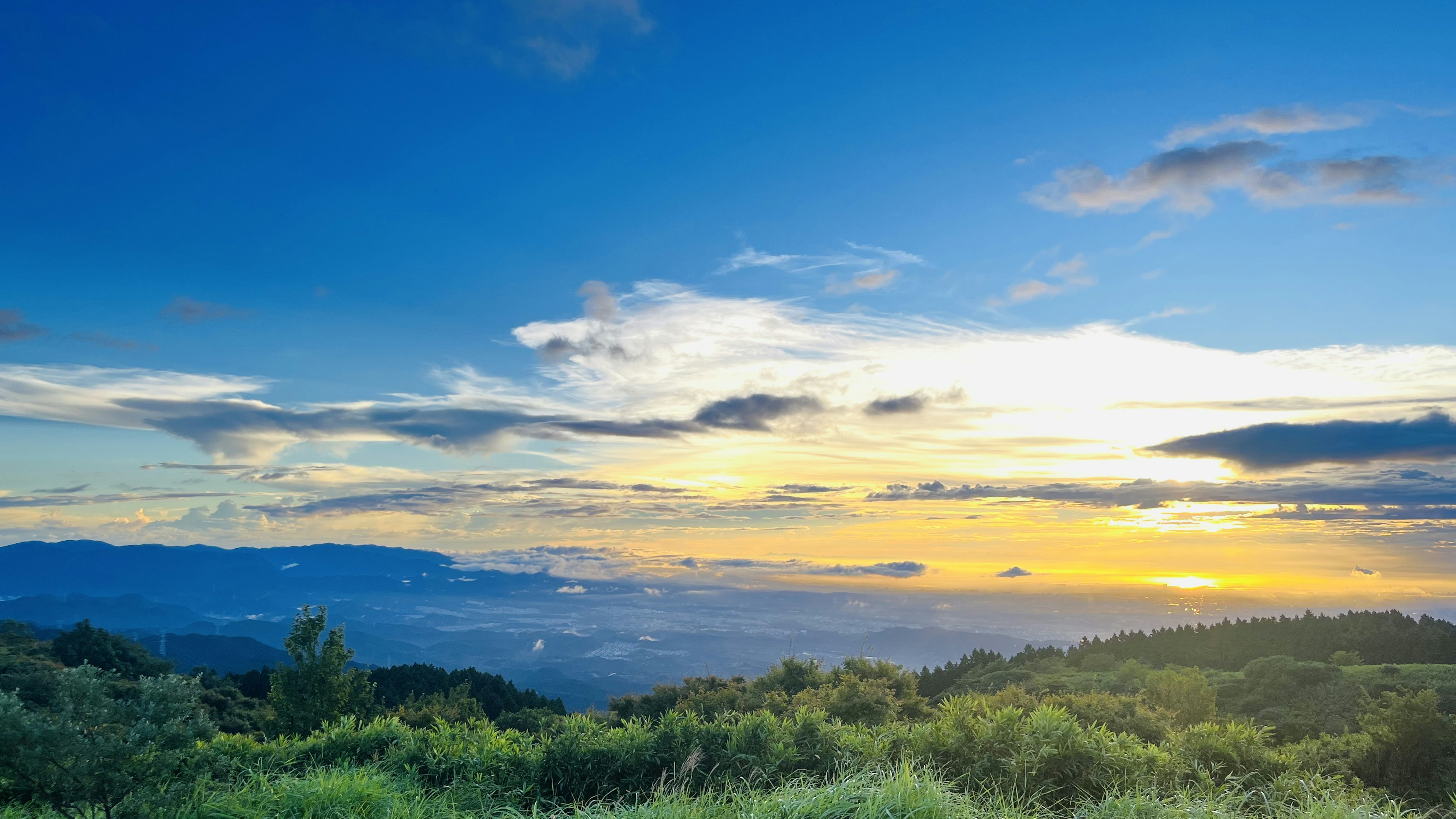 Wunderschöne Sonnenuntergangs- und blauer Himmel Landschaft mit grünen Hügeln und fernen Bergen