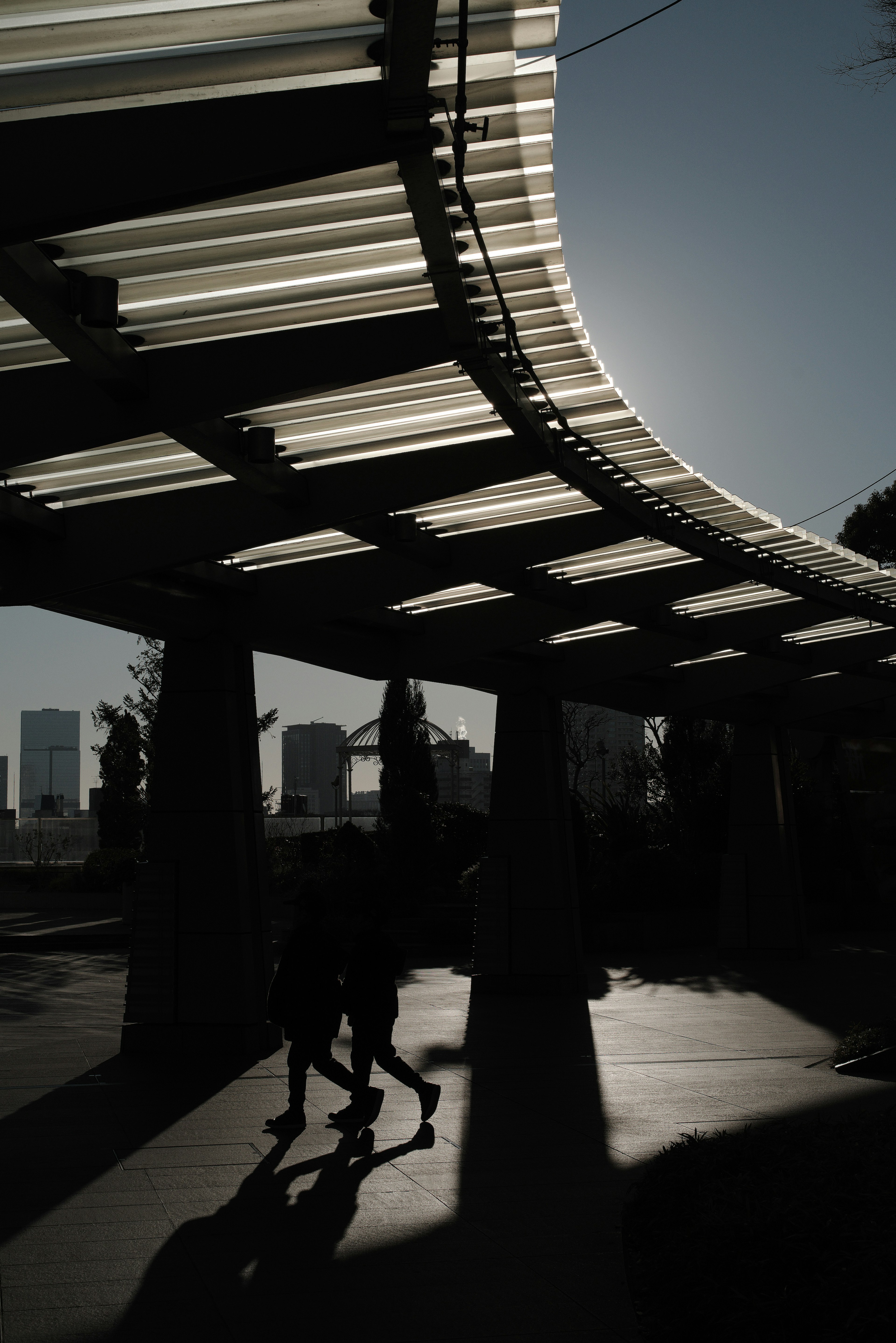 Siluetas de personas caminando bajo un techo curvado con fondo urbano y fuerte contraste