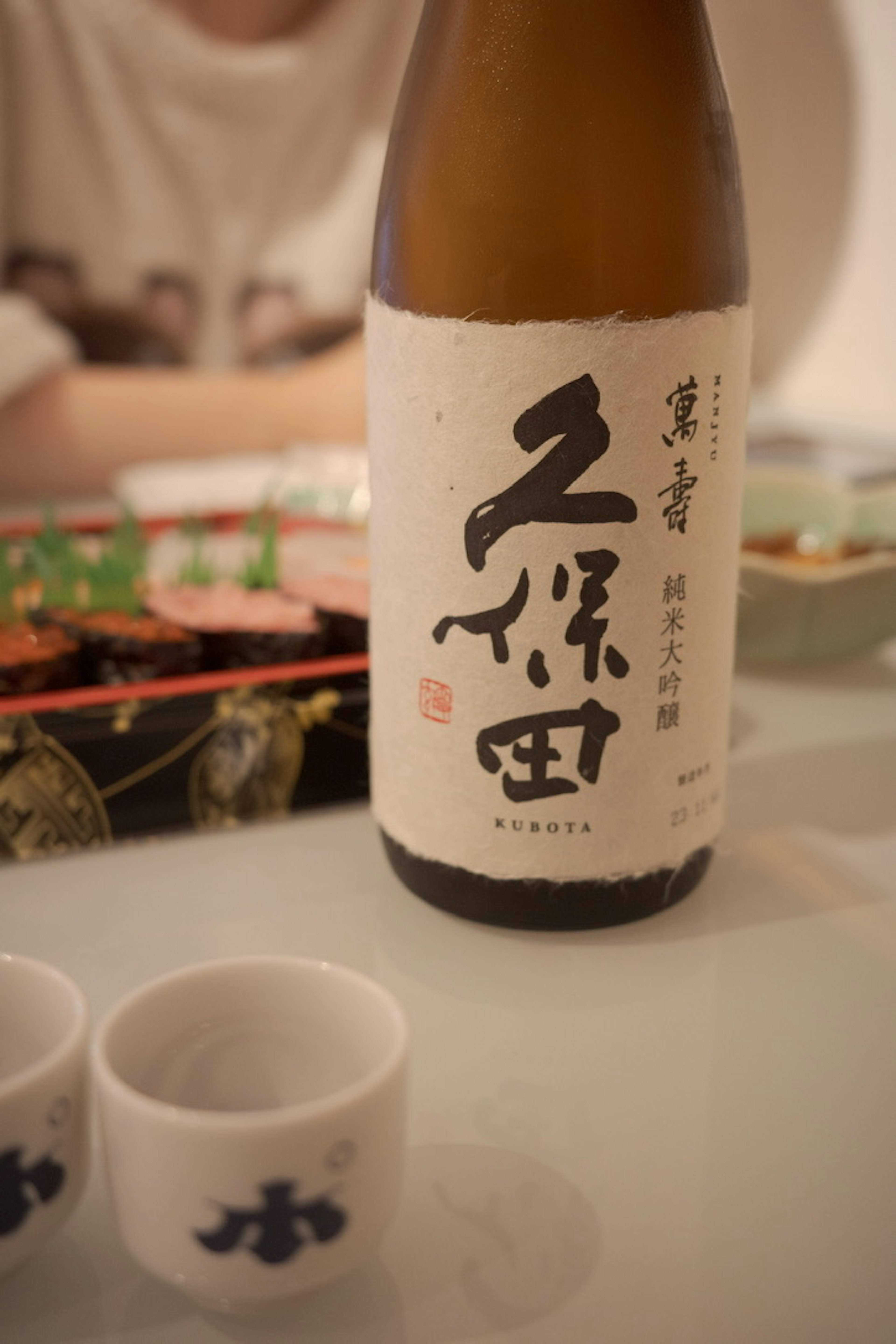 Eine Flasche Sake mit kleinen Sake-Bechern auf einem Tisch