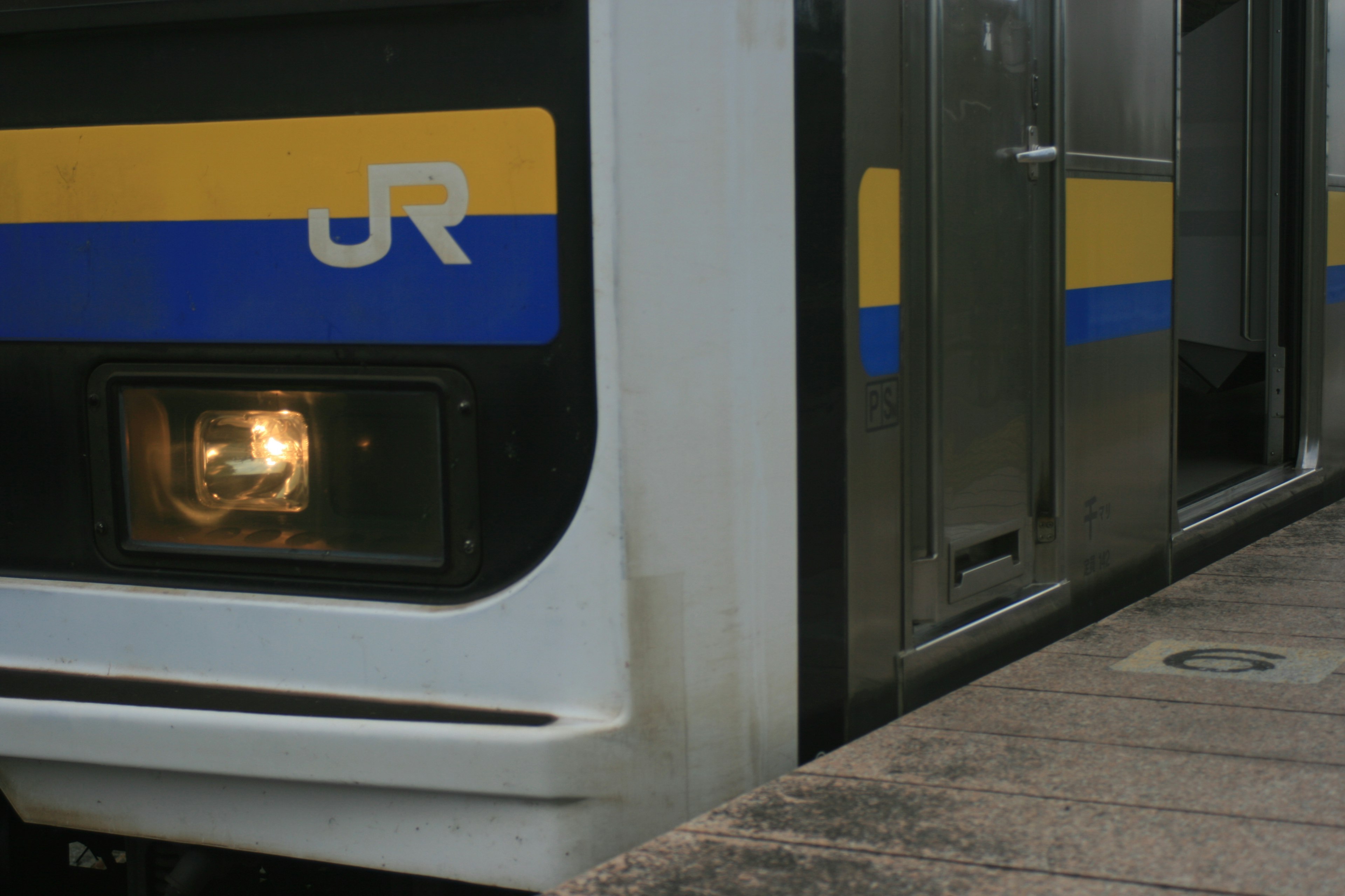 Close-up of a JR train front with a headlight and blue yellow stripes