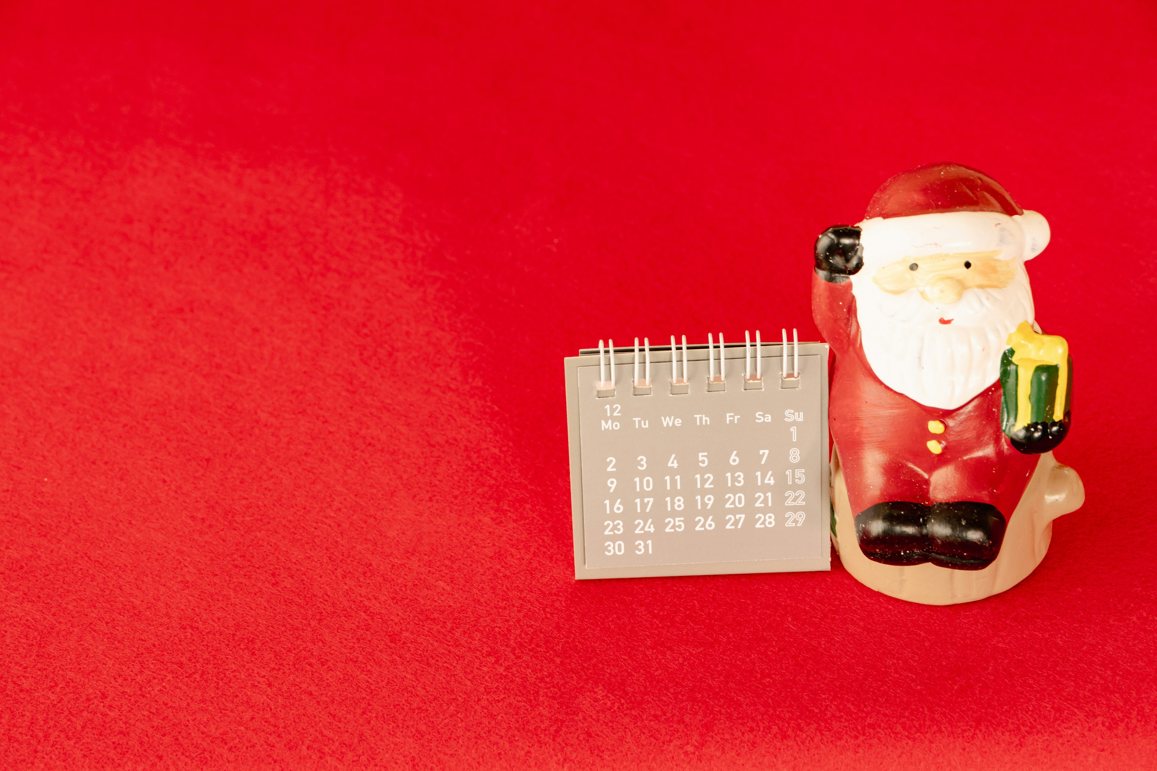 Una statuetta di Babbo Natale accanto a un calendario su uno sfondo rosso