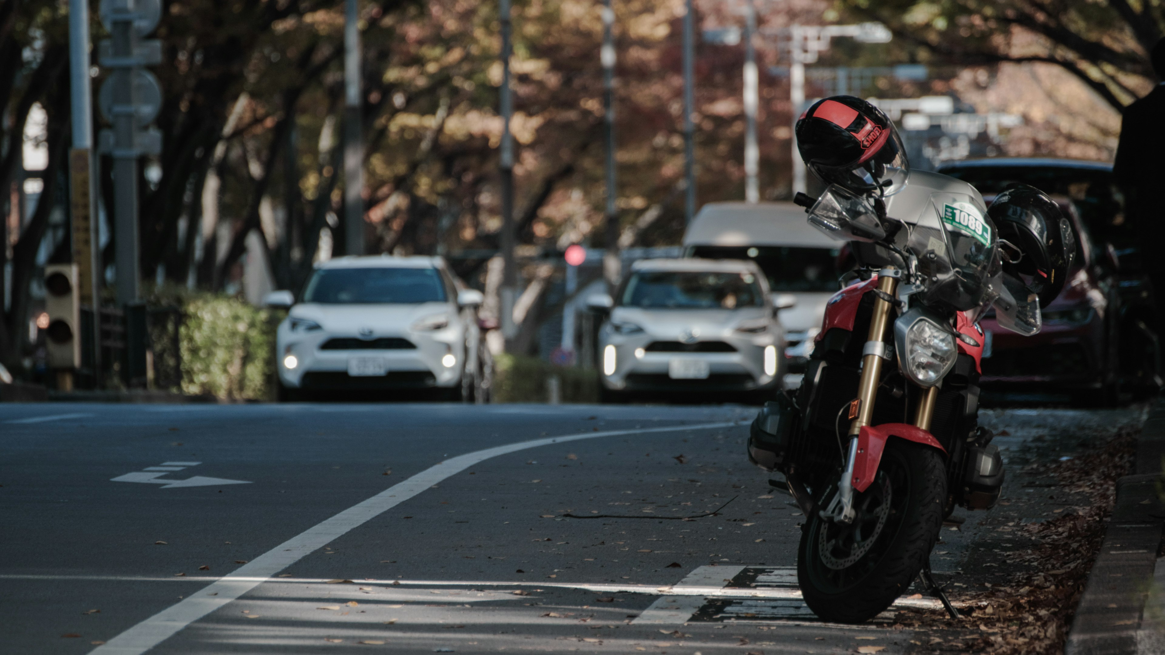 赤いバイクが並ぶ車の横に停まっている街の風景