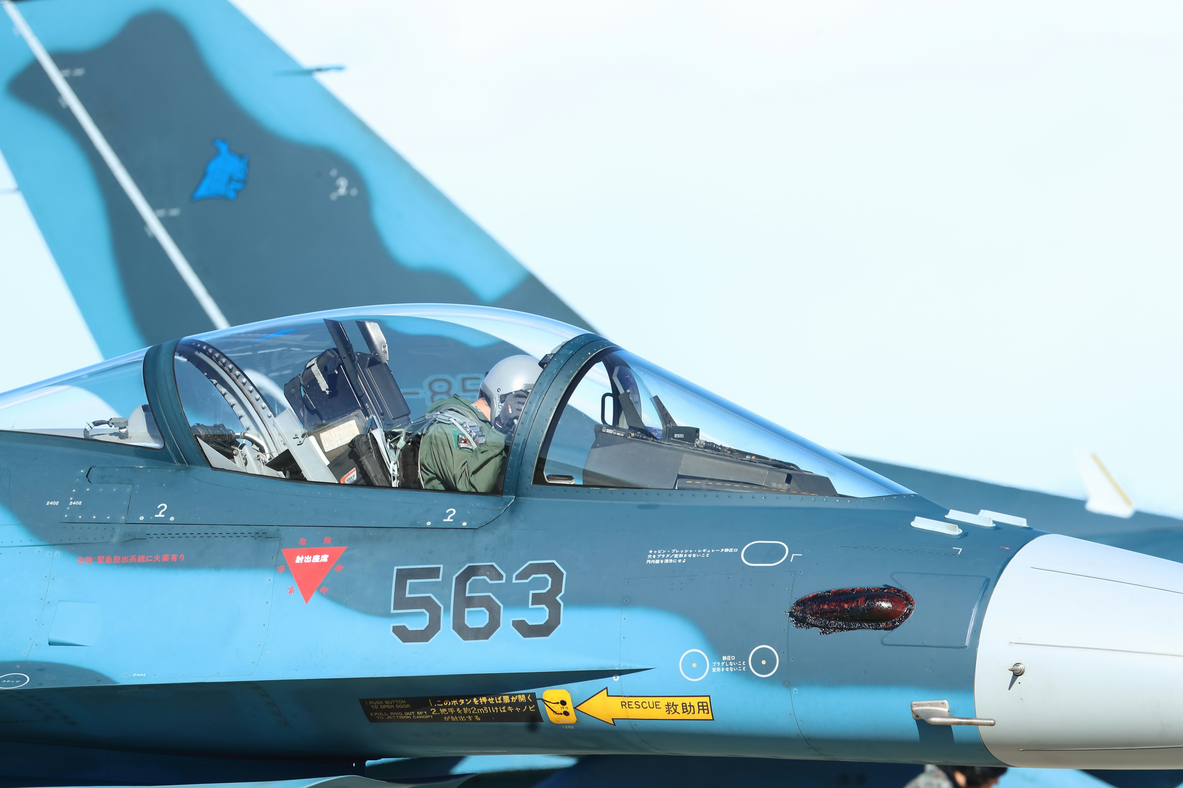 Seitenansicht des Cockpits eines blau und schwarz camouflierten Kampfjets mit einem Piloten