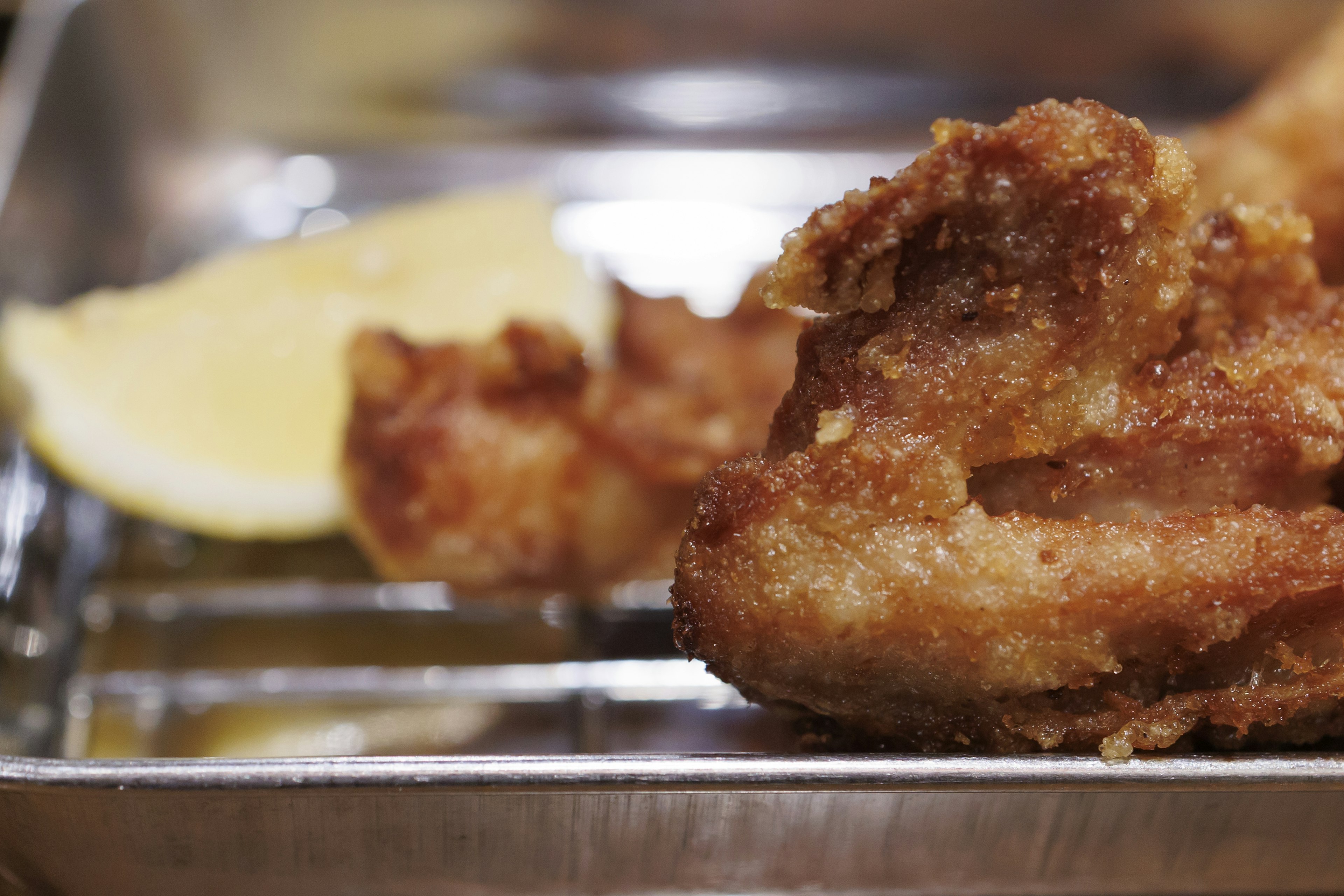 Pollo frito con una rodaja de limón servido en una bandeja metálica