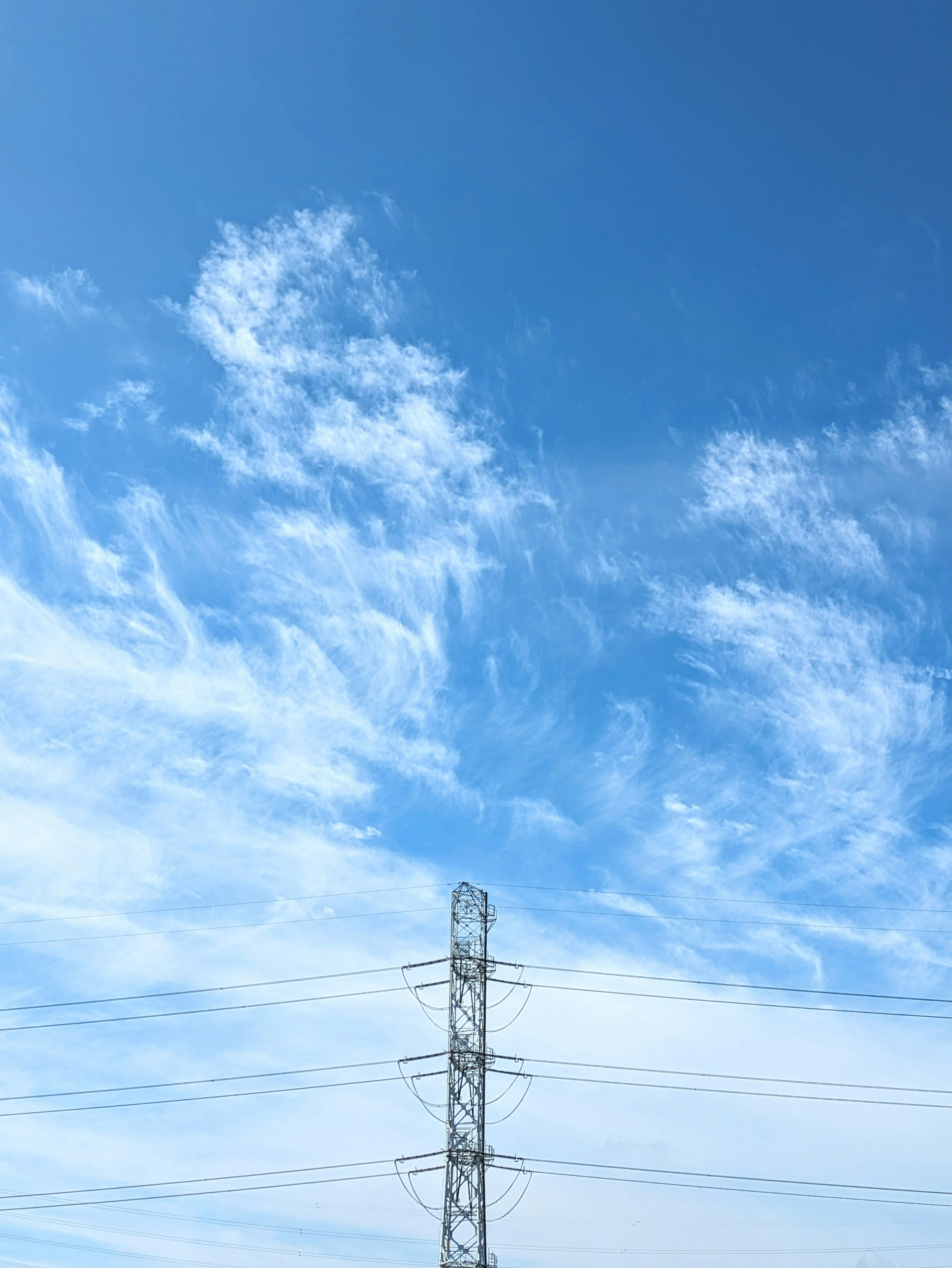 A landscape with a bright blue sky and white clouds featuring a power line tower