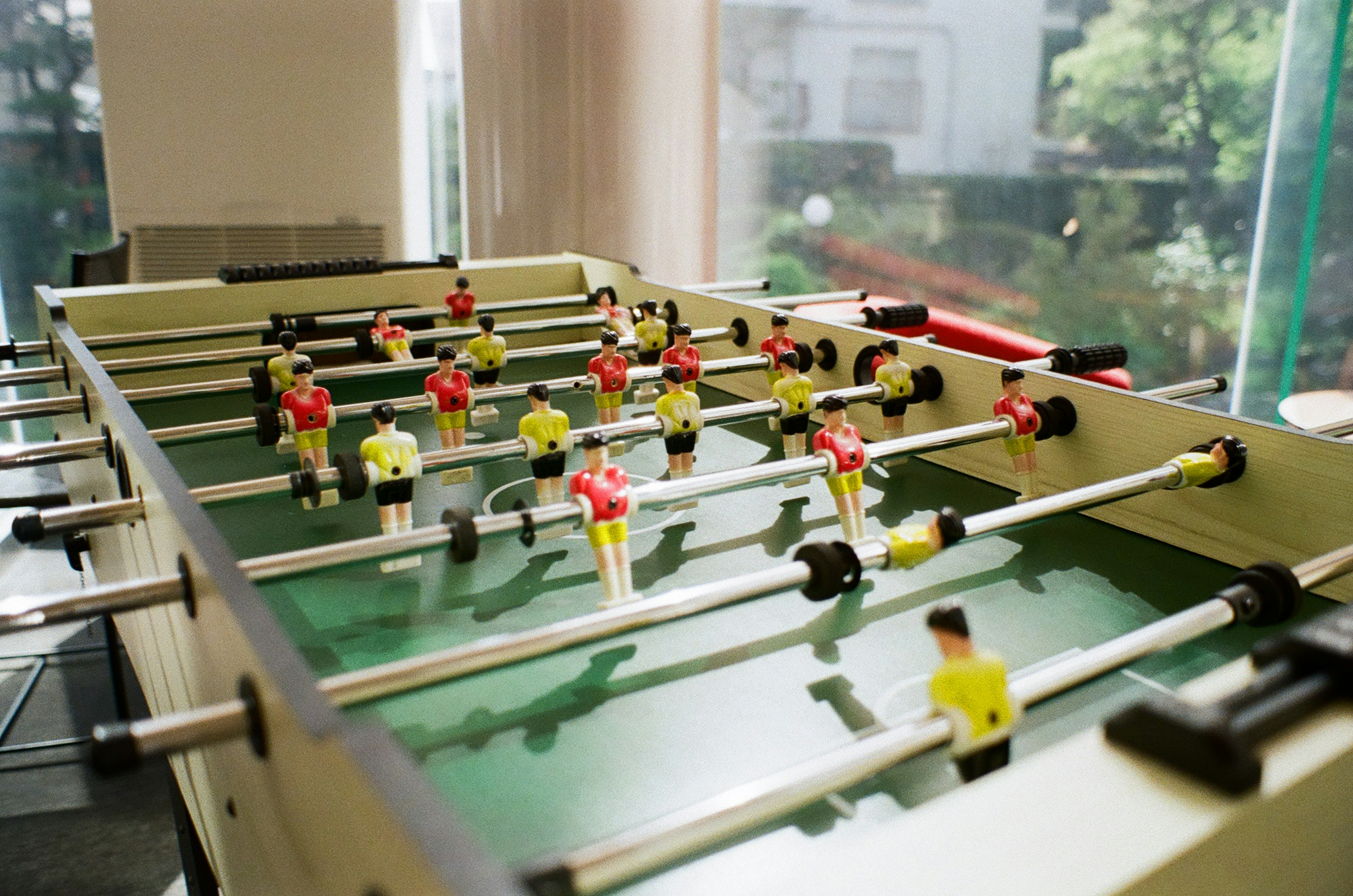 Meja foosball dengan pemain kuning dan merah yang diposisikan di lapangan hijau