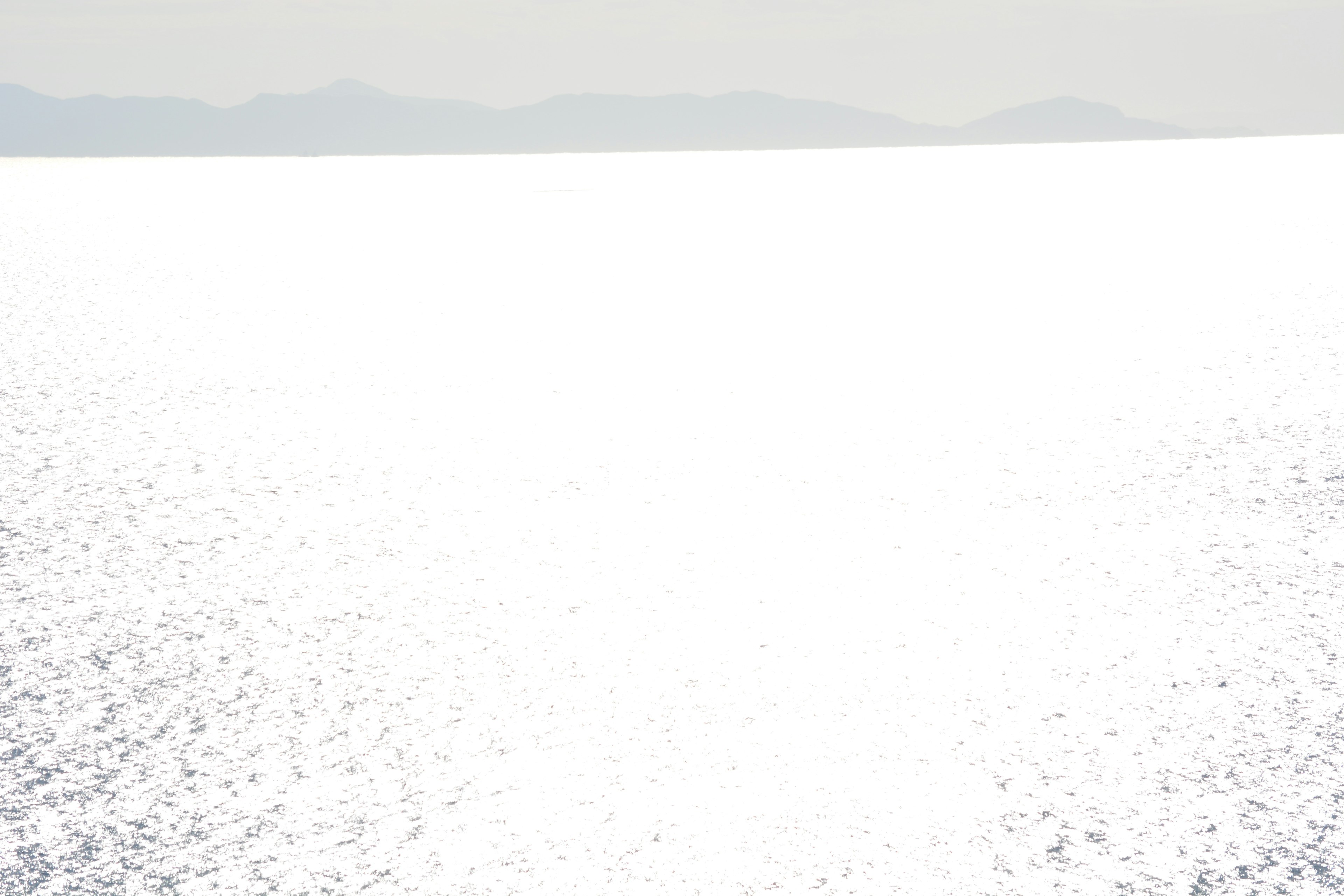 Glare from the ocean reflecting sunlight with distant mountains