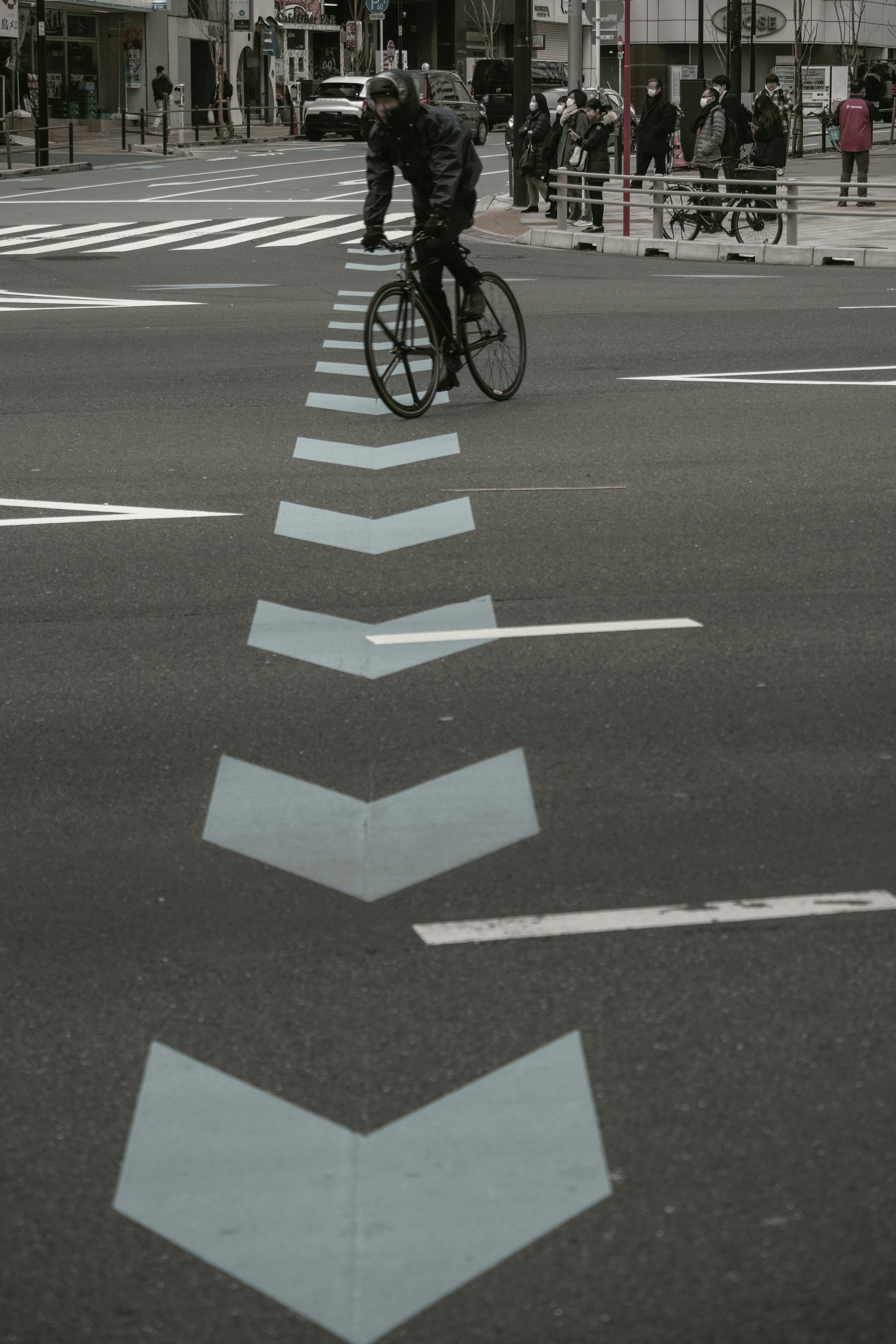 A cyclist riding over blue arrow markings on a street in an urban setting