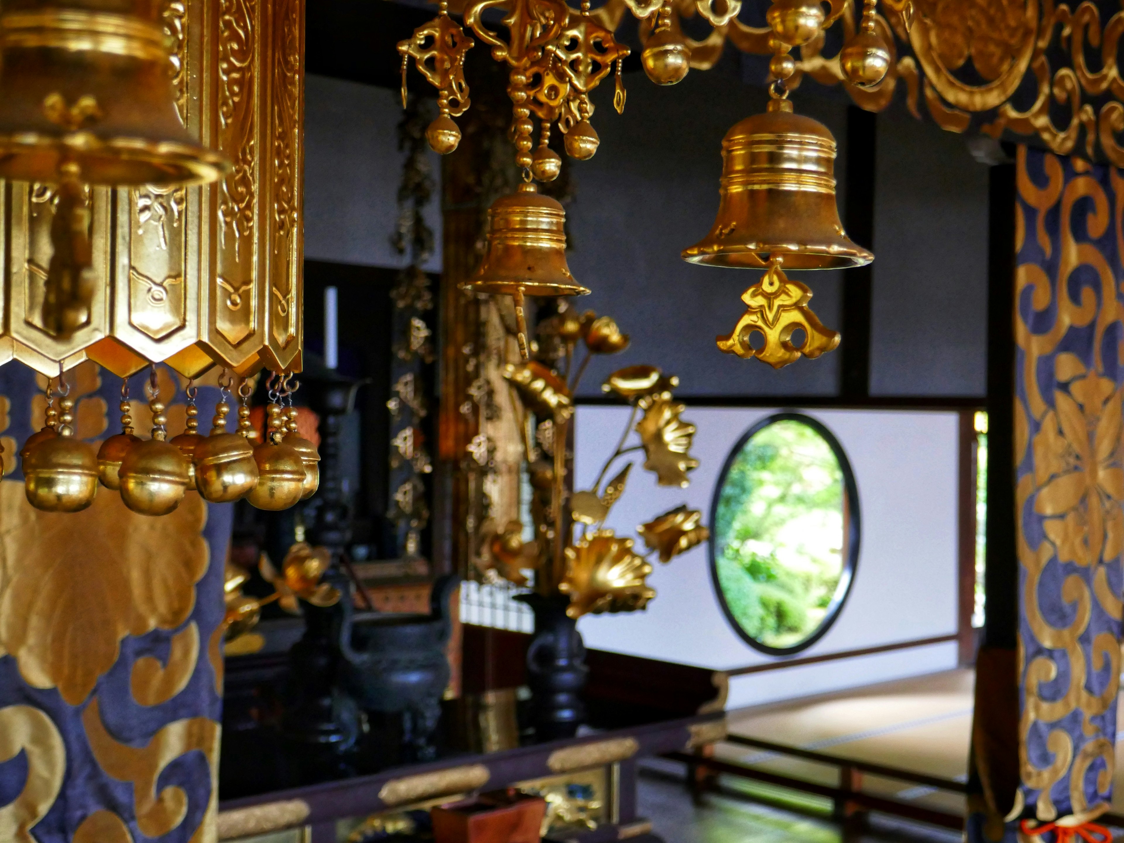 Interior of a traditional Japanese building with golden decorations and a round window revealing greenery