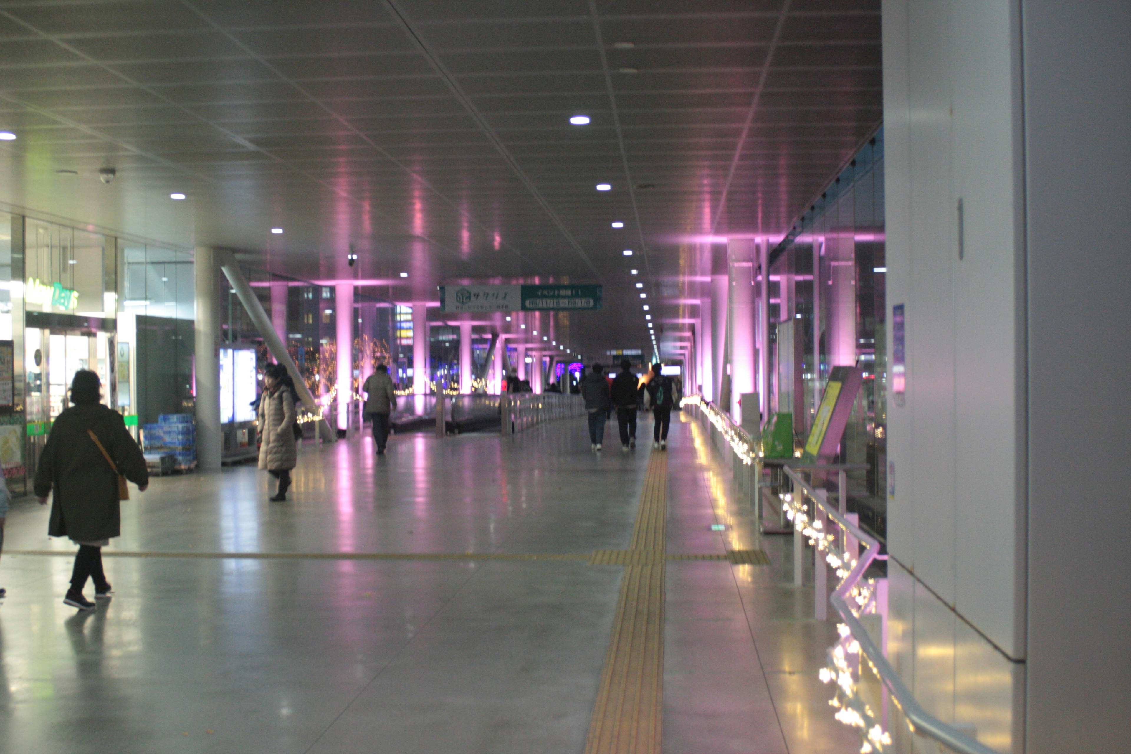 Wide corridor illuminated with bright pink lights featuring people walking