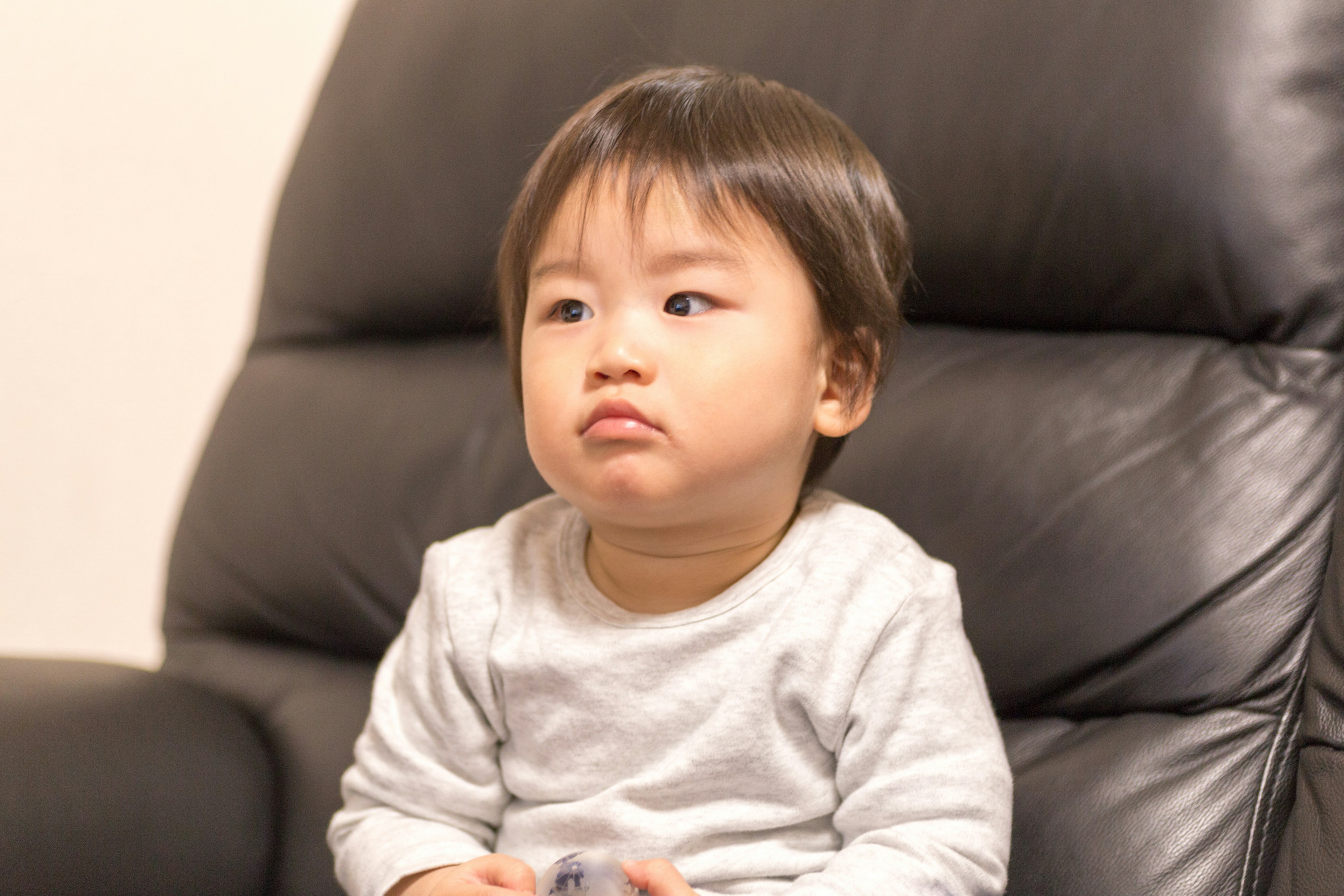 Jeune enfant assis sur un canapé noir regardant pensivement