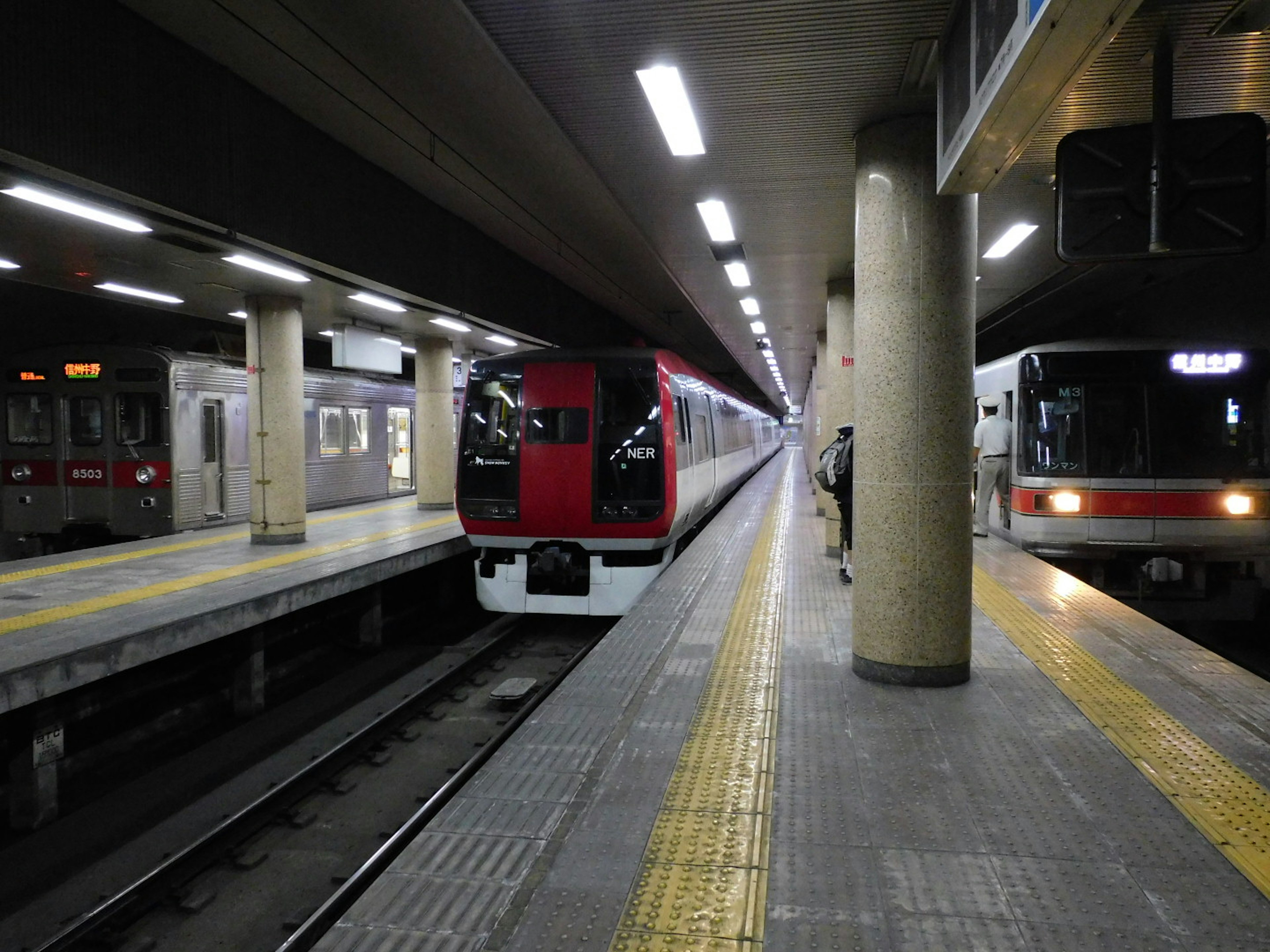 Vista de una estación de metro con un tren rojo y un tren negro en la plataforma