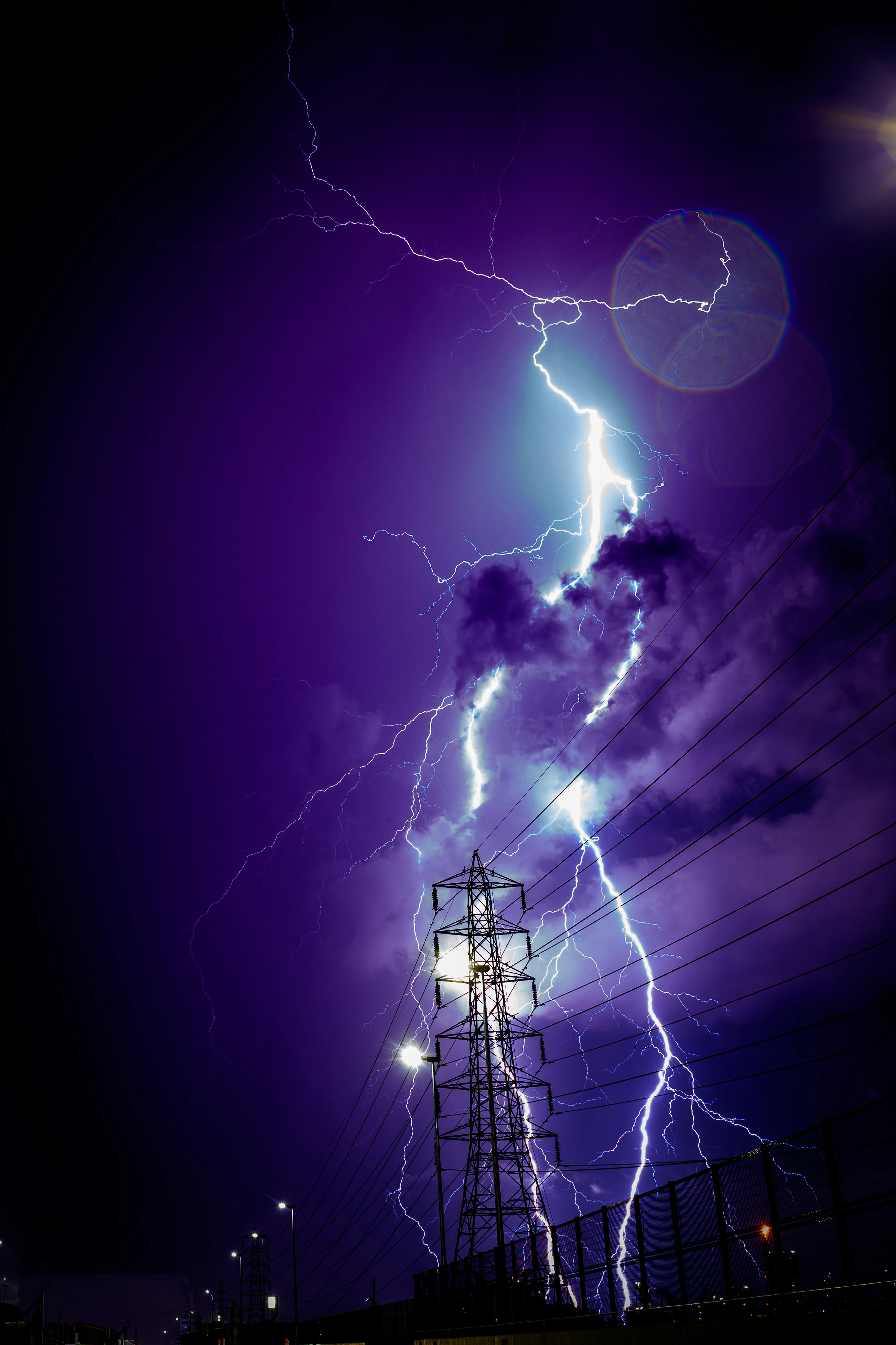 Lightning striking in a purple sky with a power pole illuminated