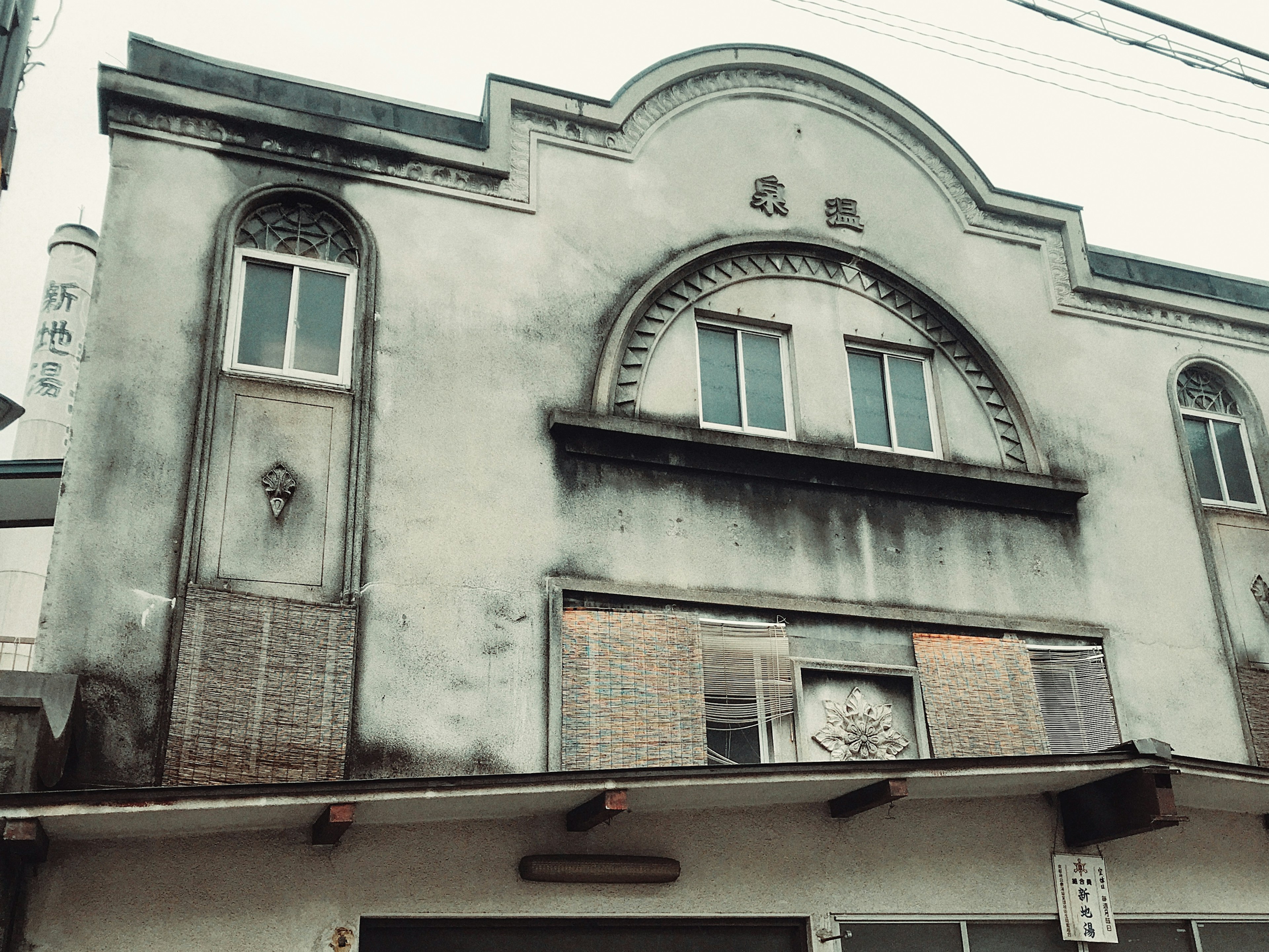 Fassade eines alten Gebäudes mit Fenstern, verwitterten grauen Wänden, dekorativen Bogenmerkmalen