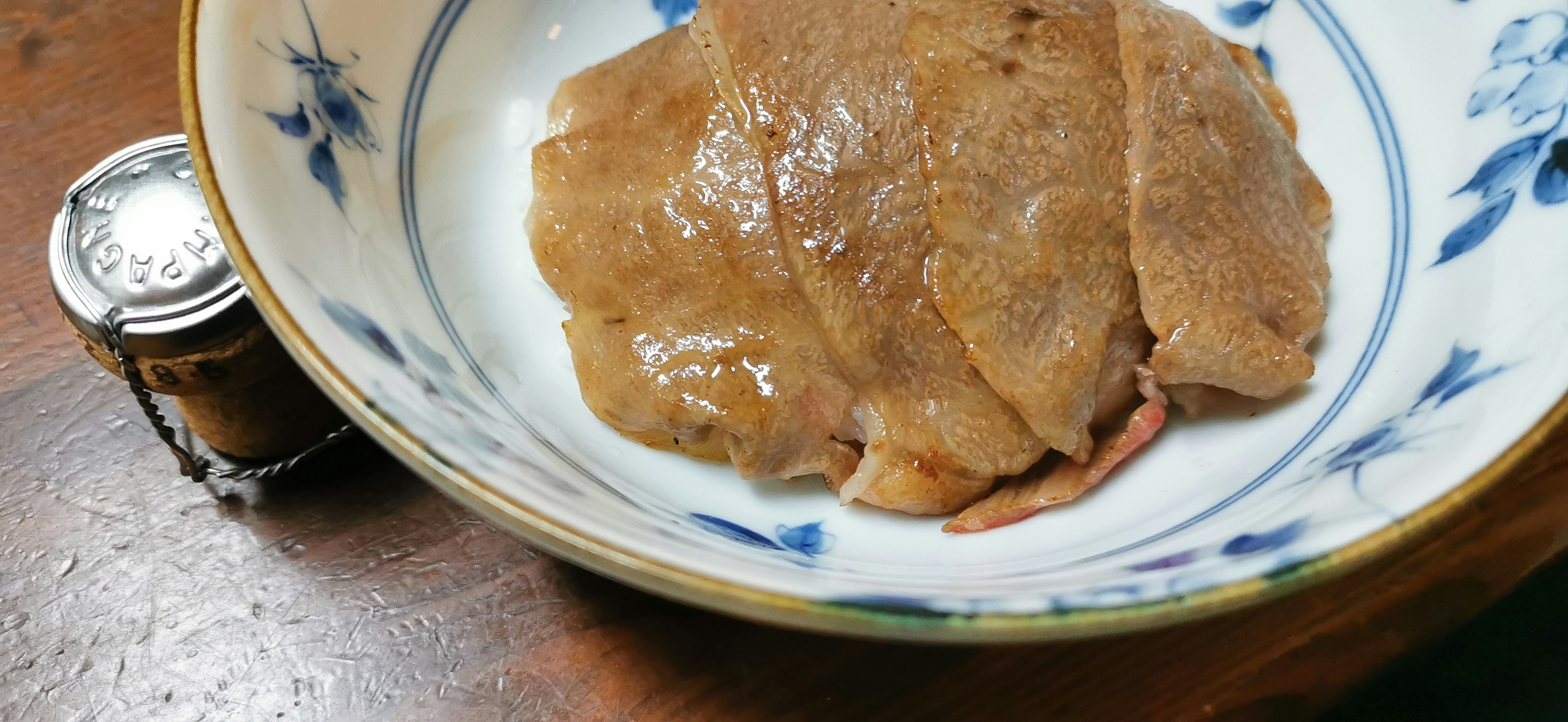 Carne en rodajas servida en un plato decorativo con un frasco pequeño