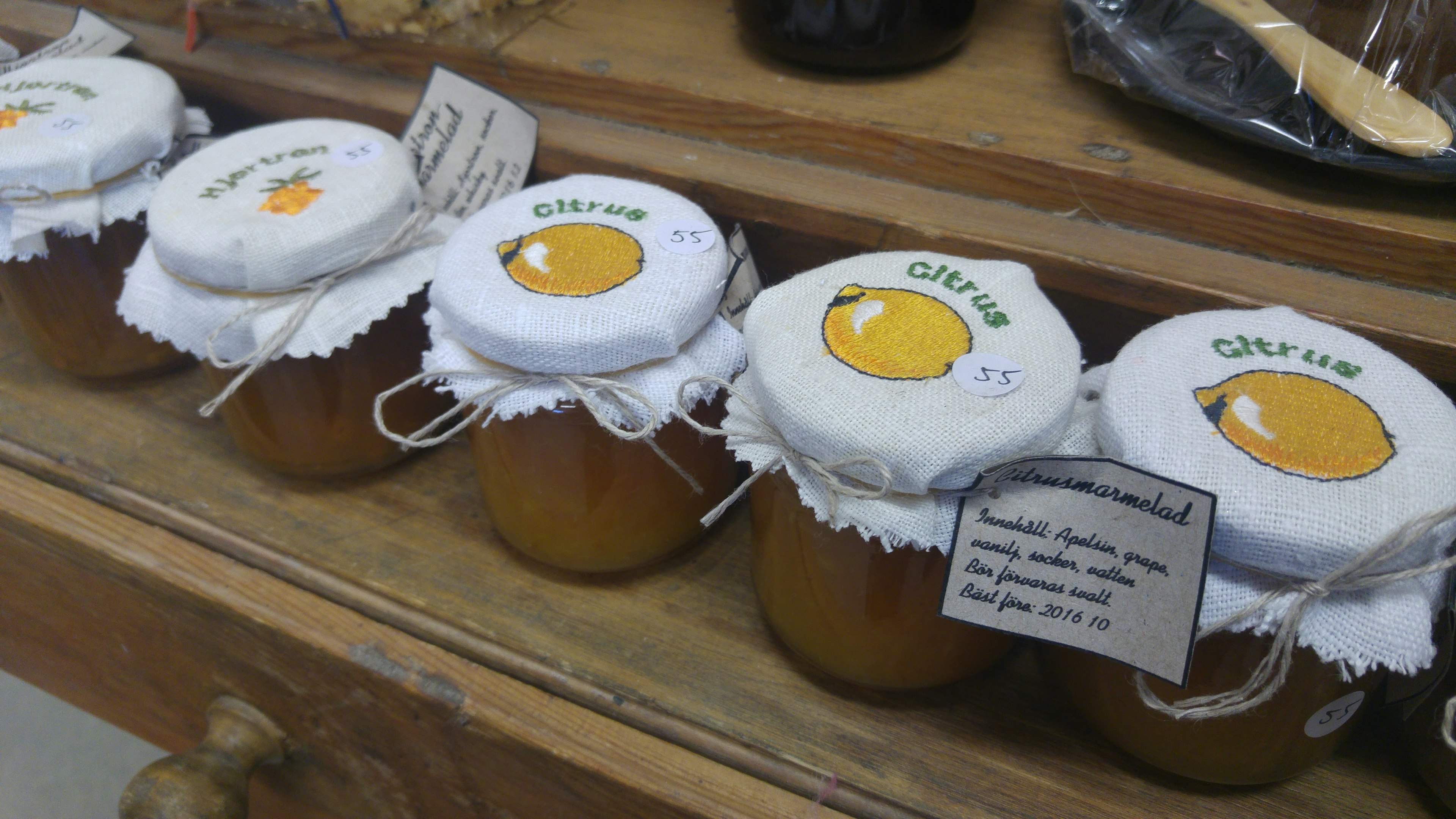 Jars of jam arranged on a wooden shelf with decorative lids