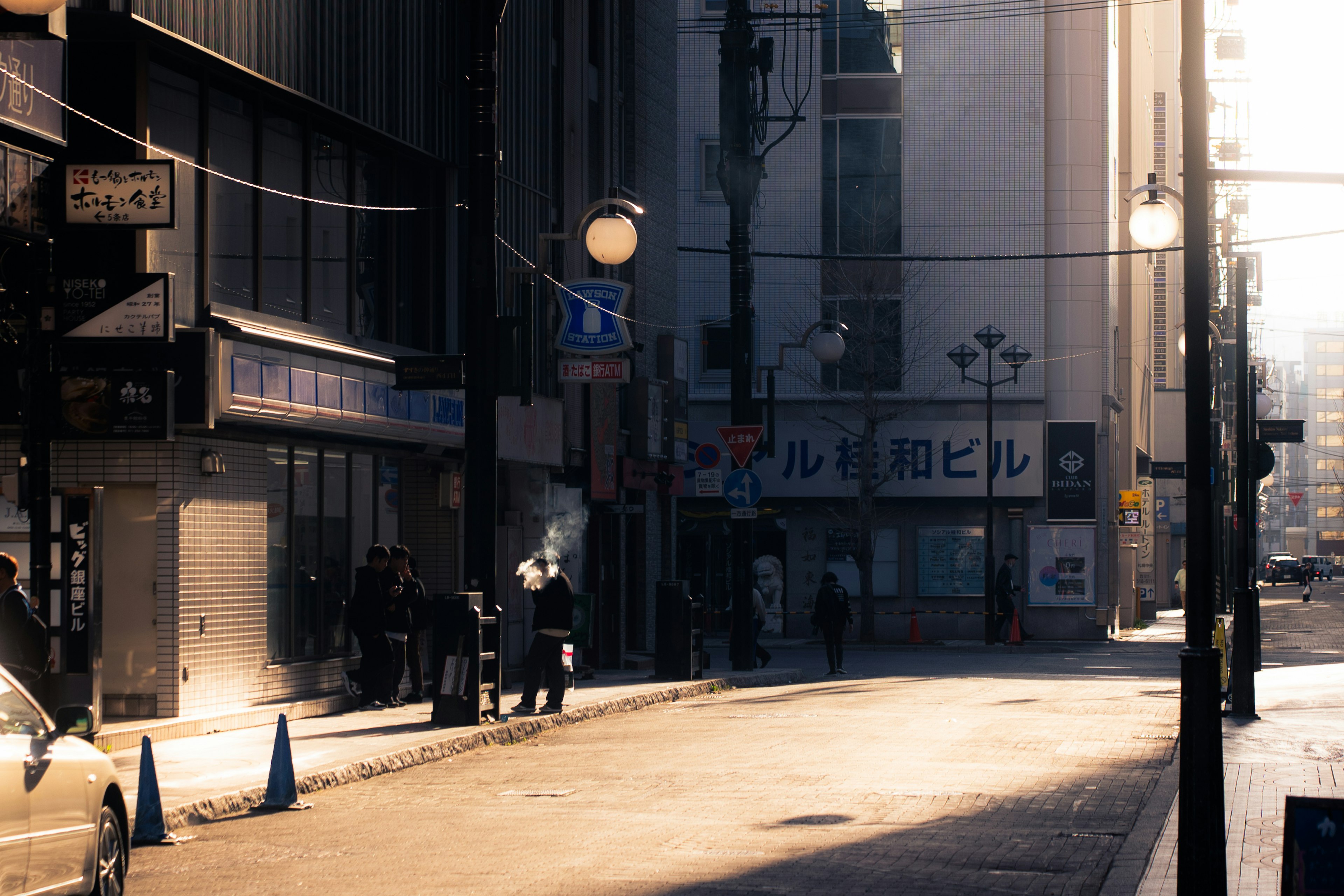 A quiet street scene with people standing and sunlight streaming