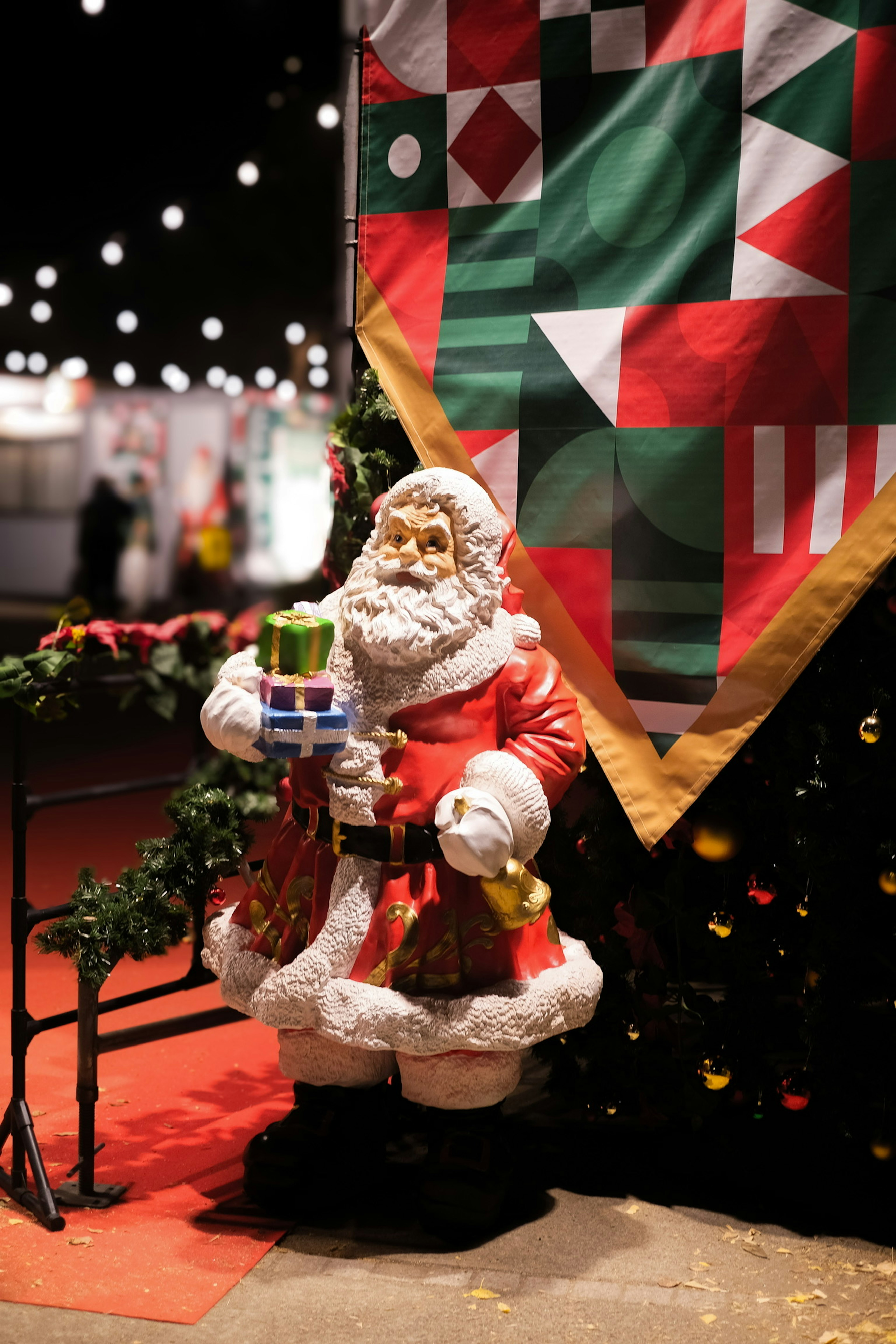 Santa Claus figurine holding gifts with colorful banner and festive lights in the background