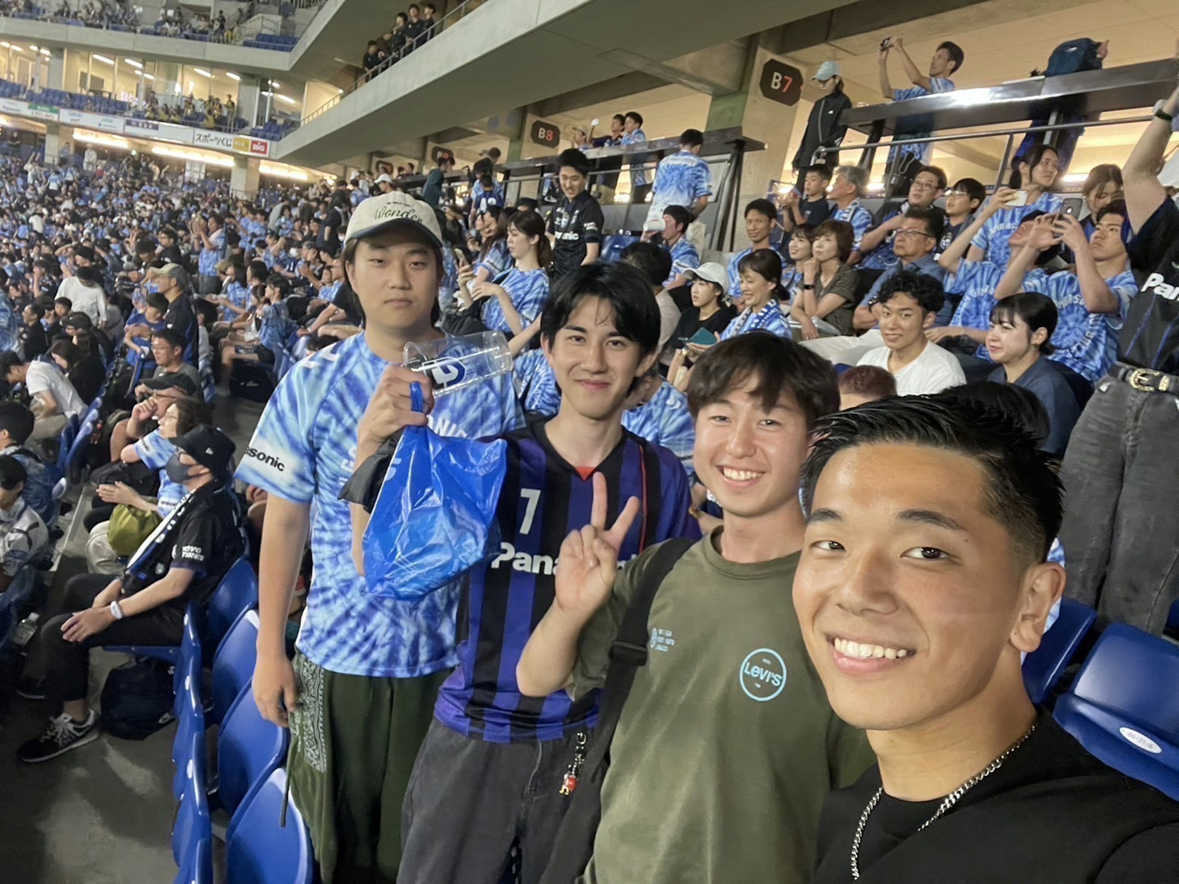 Selfie de jóvenes aficionados en un partido de fútbol con una multitud al fondo