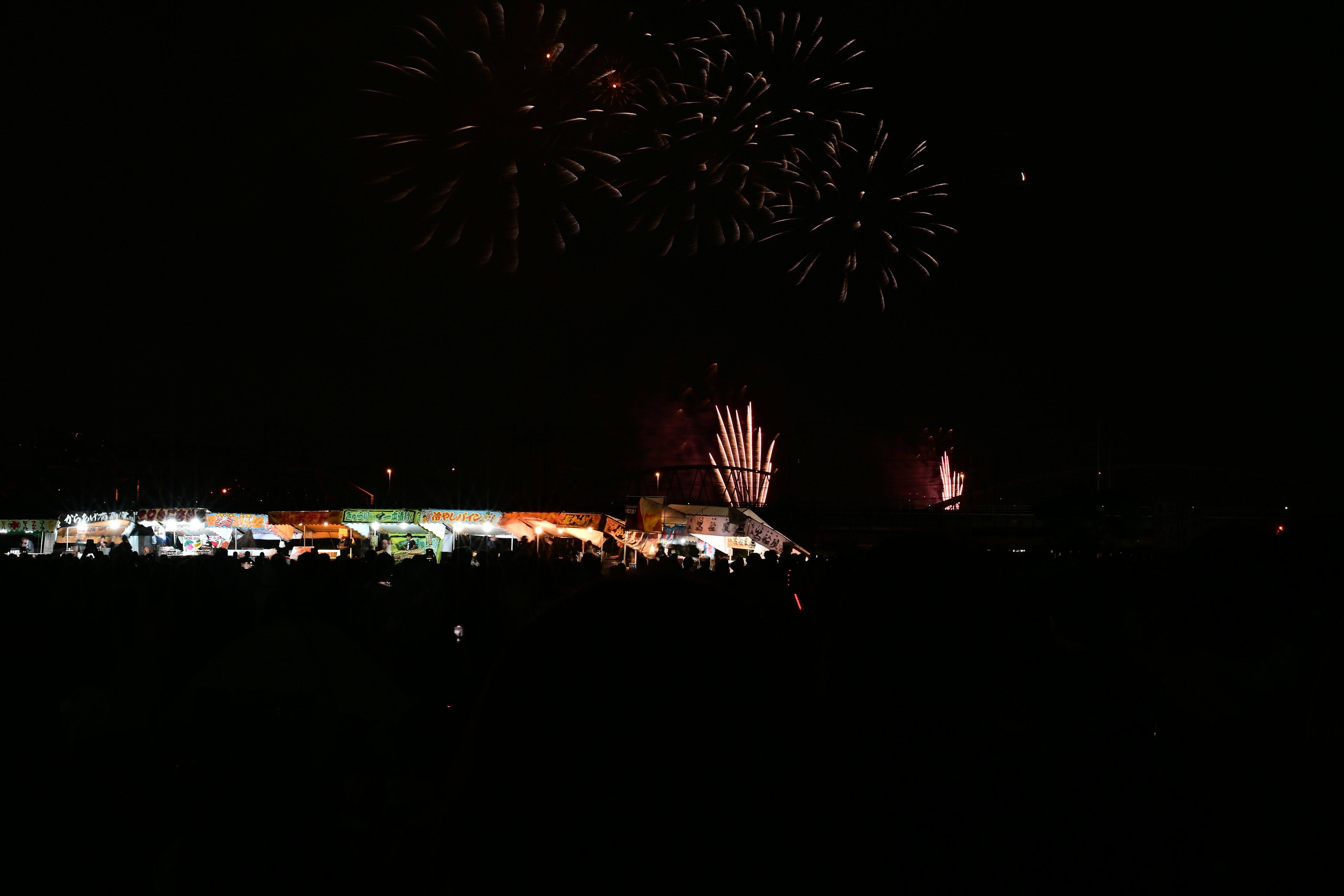 Adegan kembang api menerangi langit malam dengan lampu festival dan siluet kerumunan