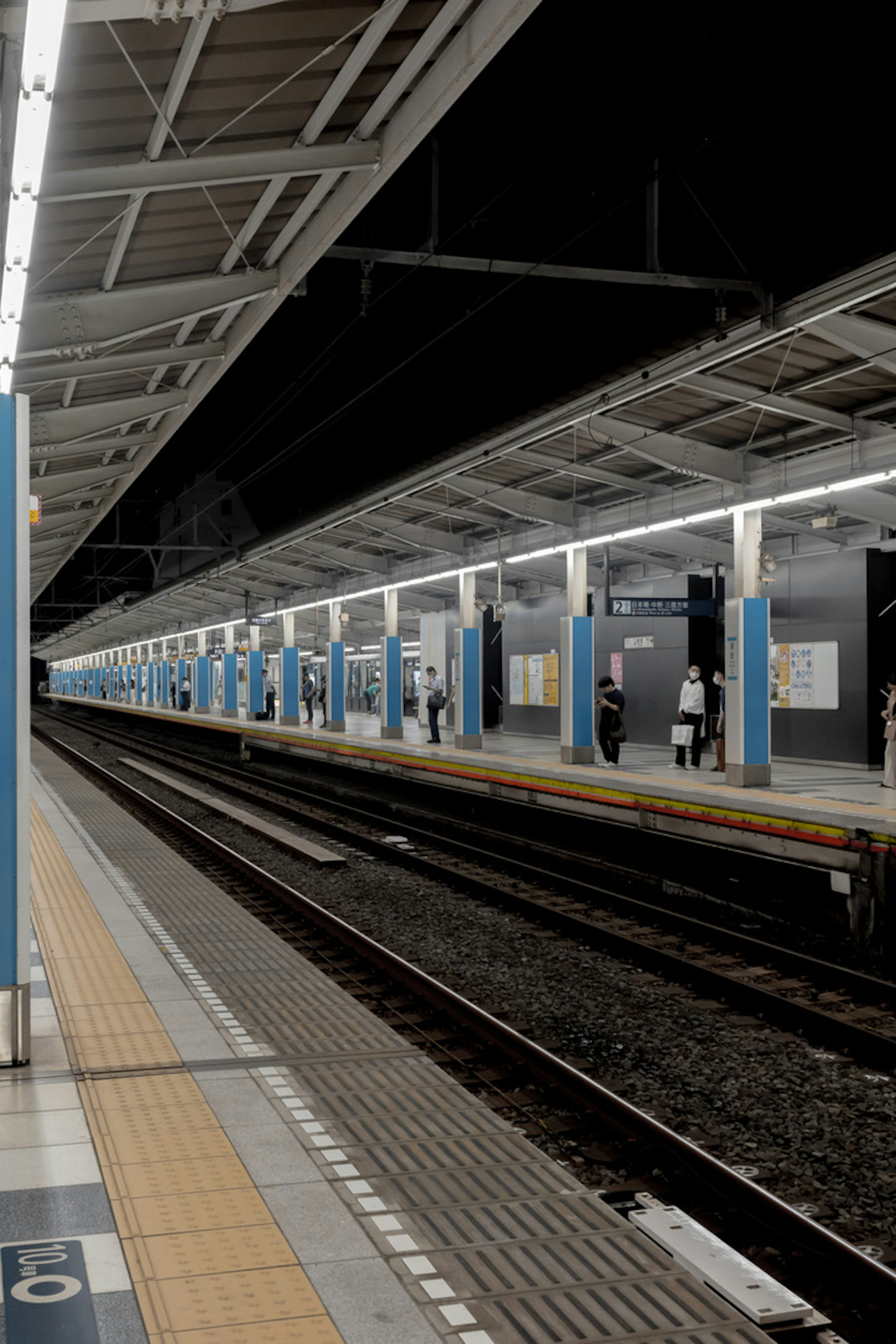 Vista notturna di una piattaforma ferroviaria con binari e colonne blu