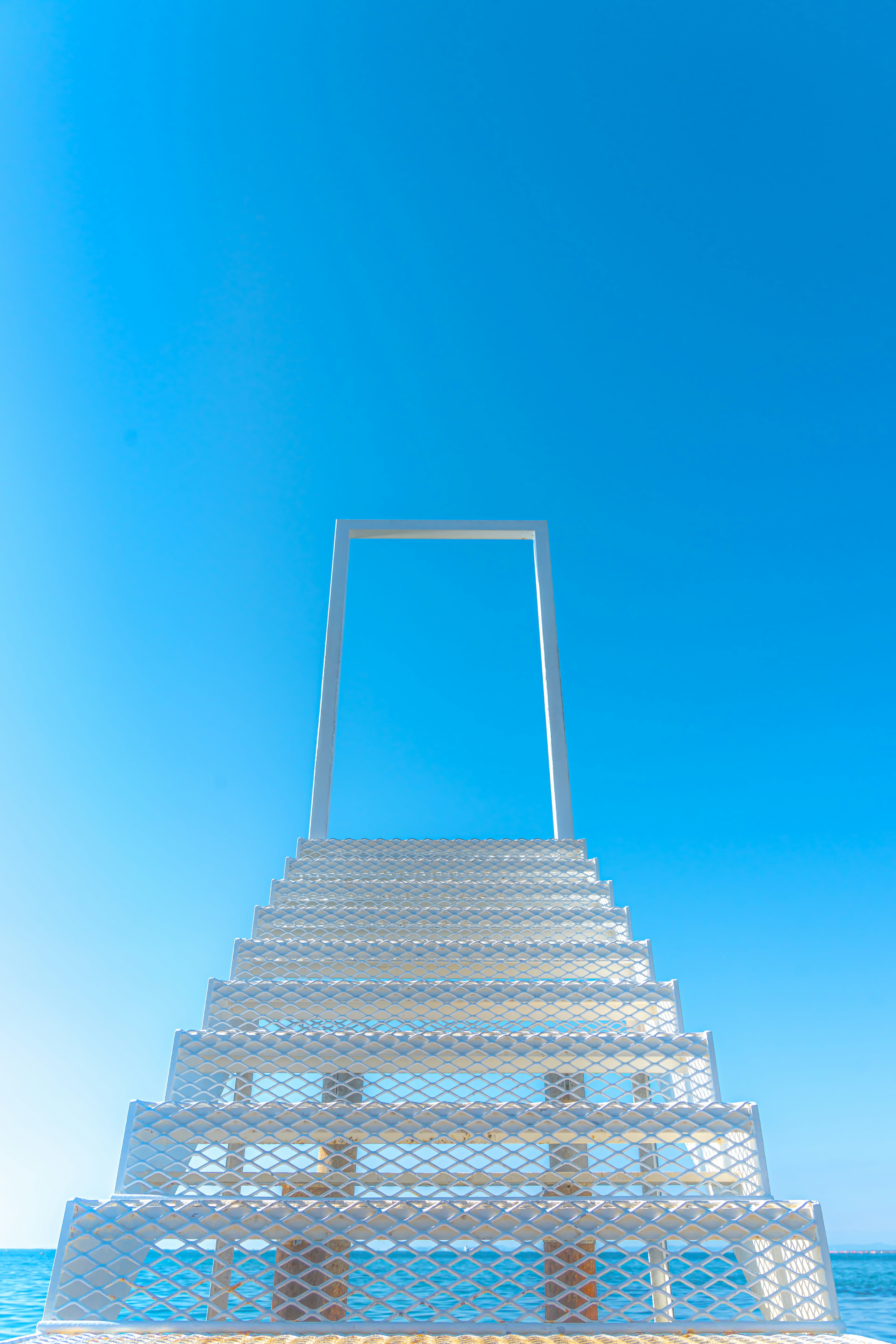 Una escalera blanca que lleva a un marco rectangular contra un cielo azul