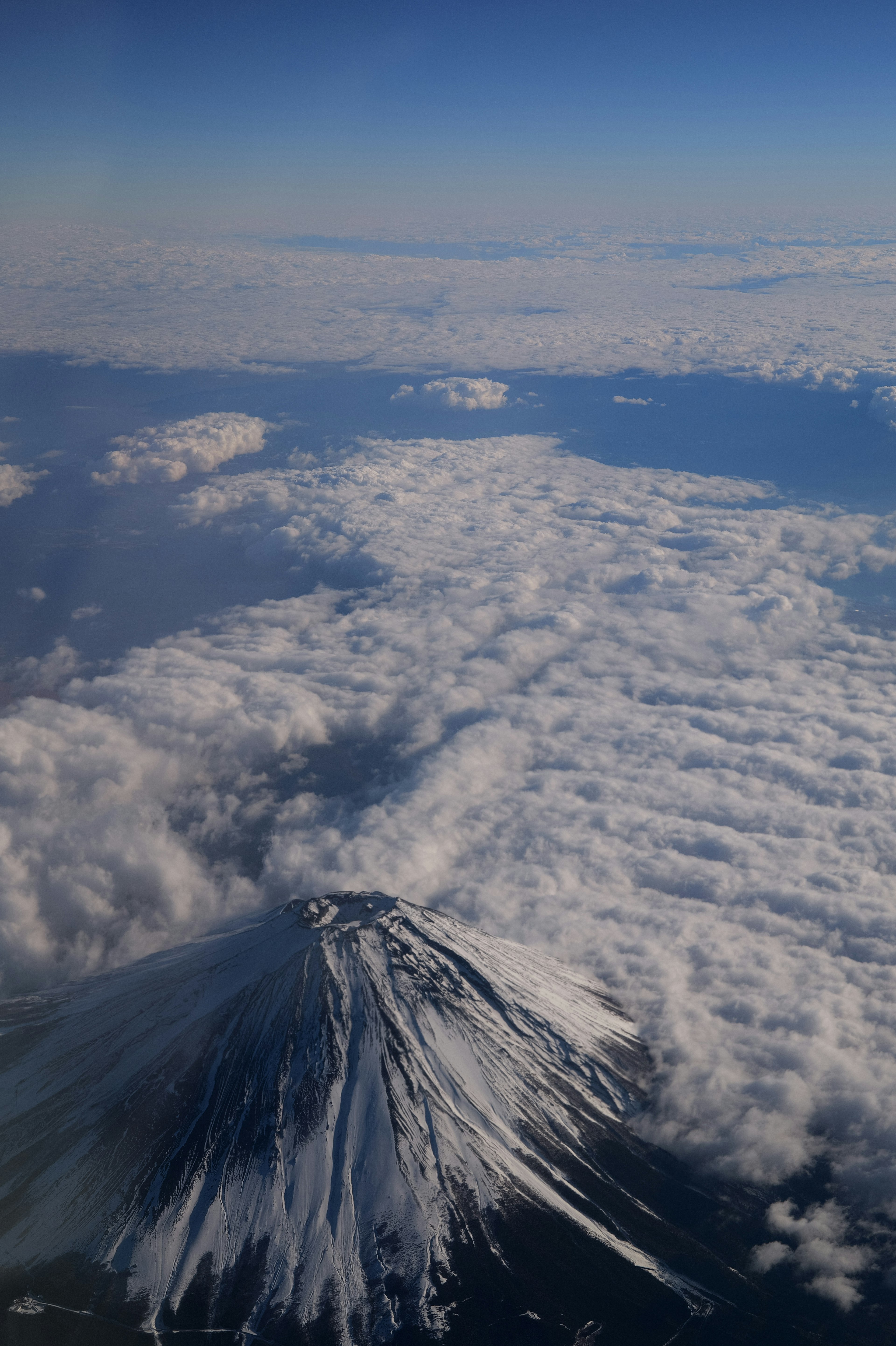 Puncak bersalju Gunung Fuji menjulang di atas lautan awan di langit biru yang cerah