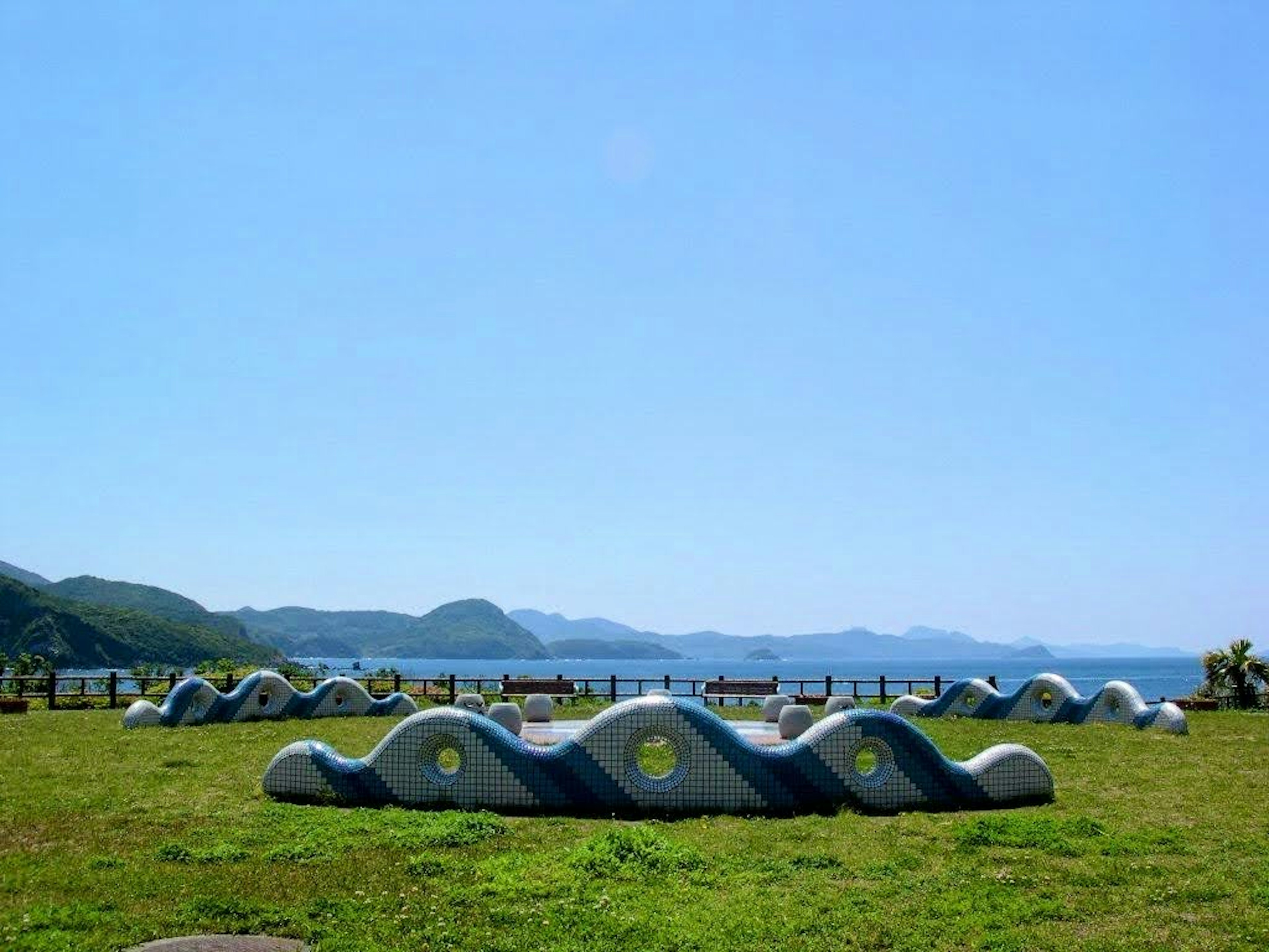 青空の下にある波状の石の彫刻と海の景色