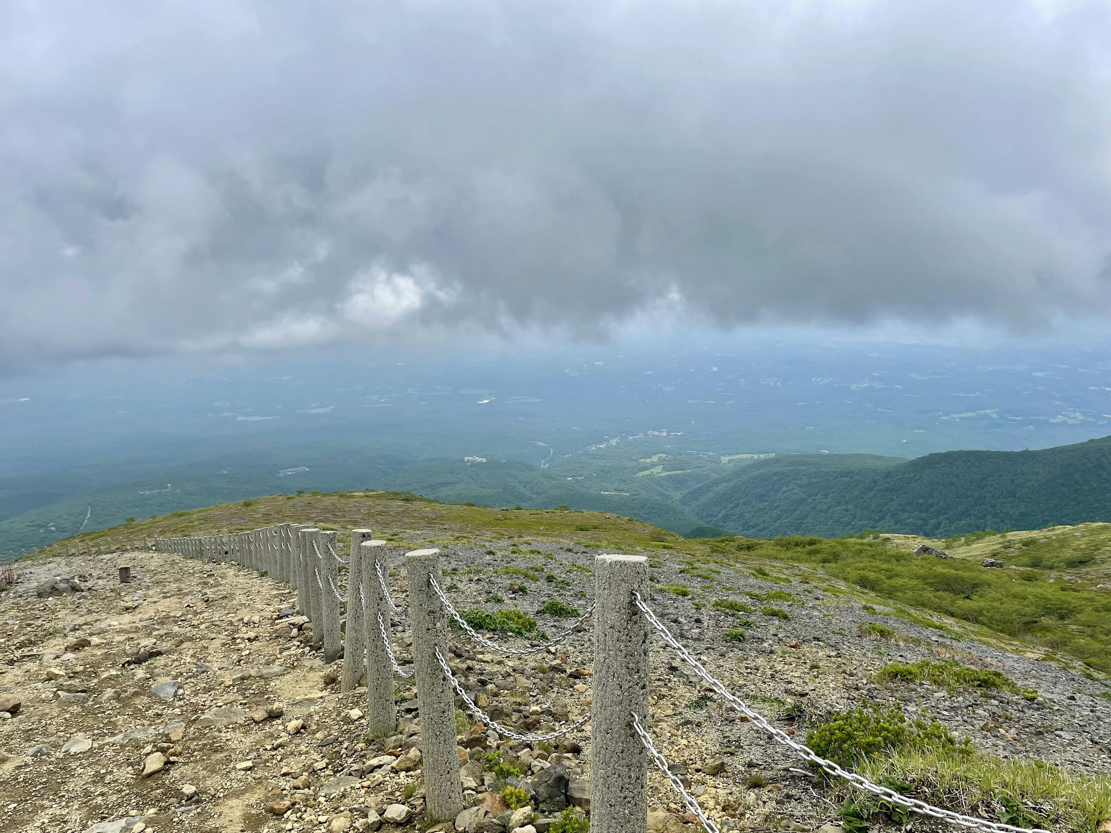 Una vista panoramica da una cima montuosa con cielo nuvoloso e un sentiero roccioso fiancheggiato da una recinzione