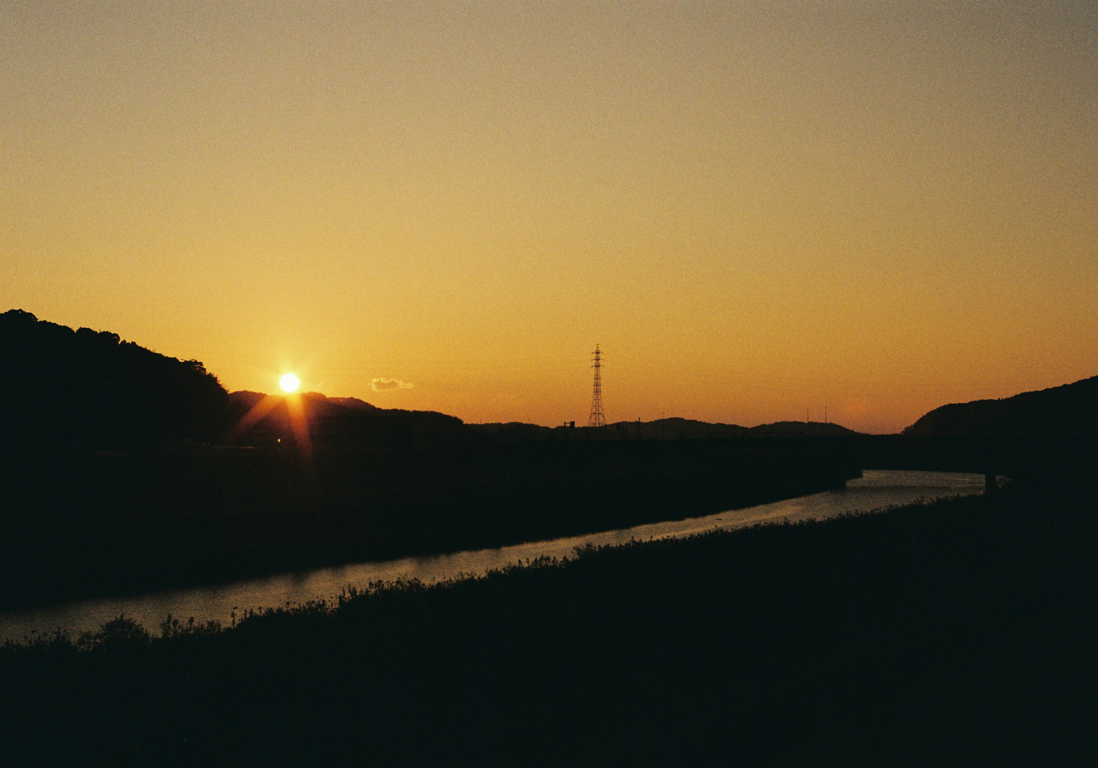 Coucher de soleil sur une rivière avec des silhouettes de collines et une surface d'eau calme