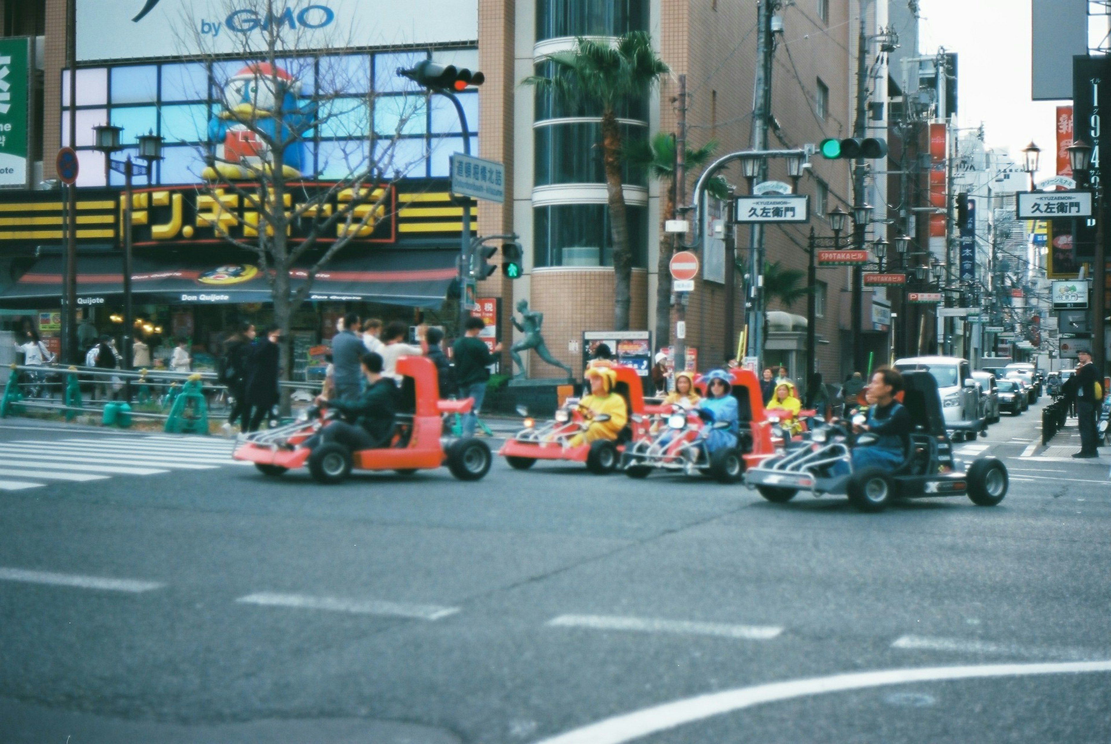 Szene von Menschen, die Go-Karts an einer Kreuzung mit Geschäftsgebäuden fahren