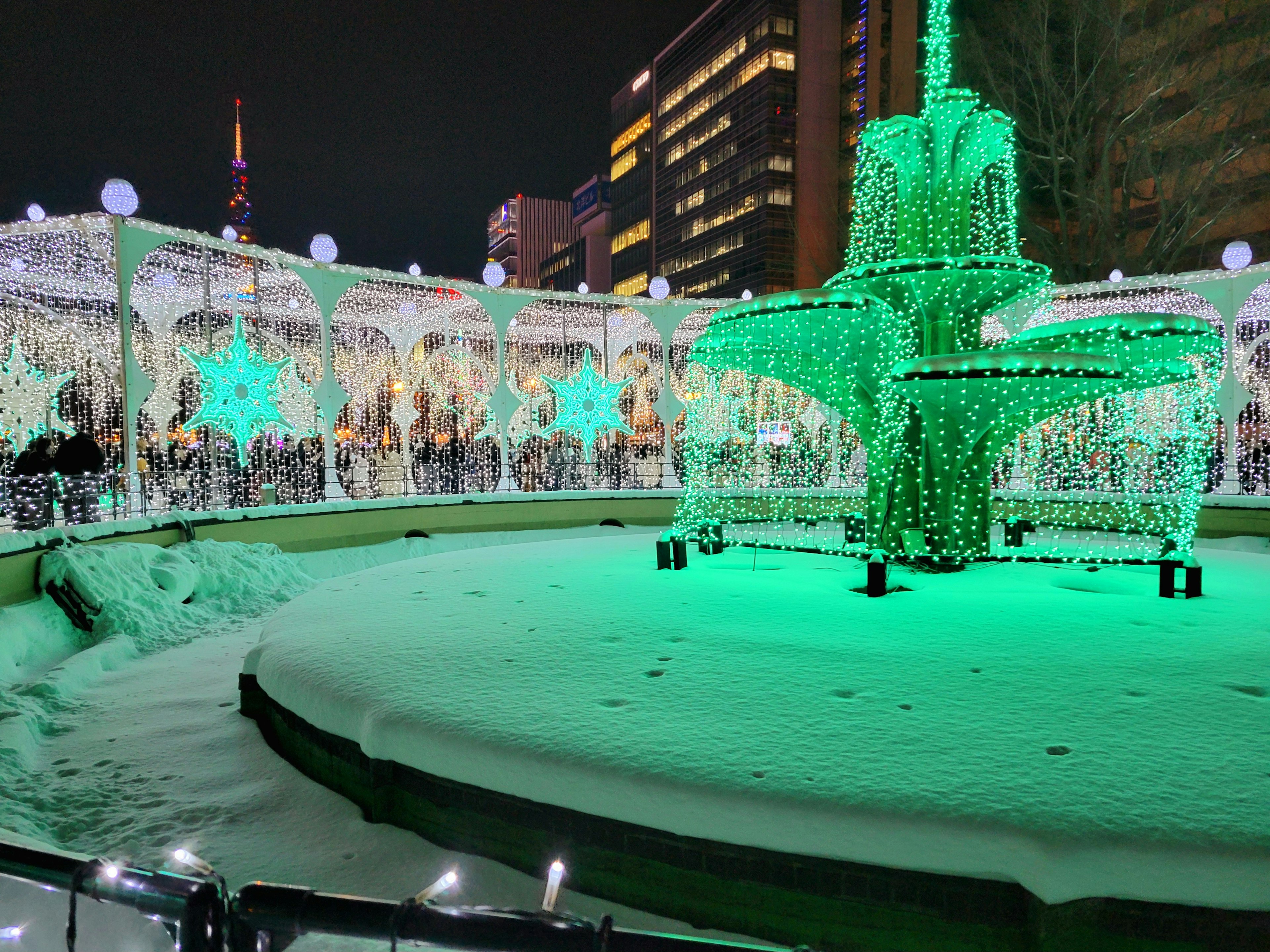 夜に輝く緑色のイルミネーションが施された噴水と雪に覆われた広場