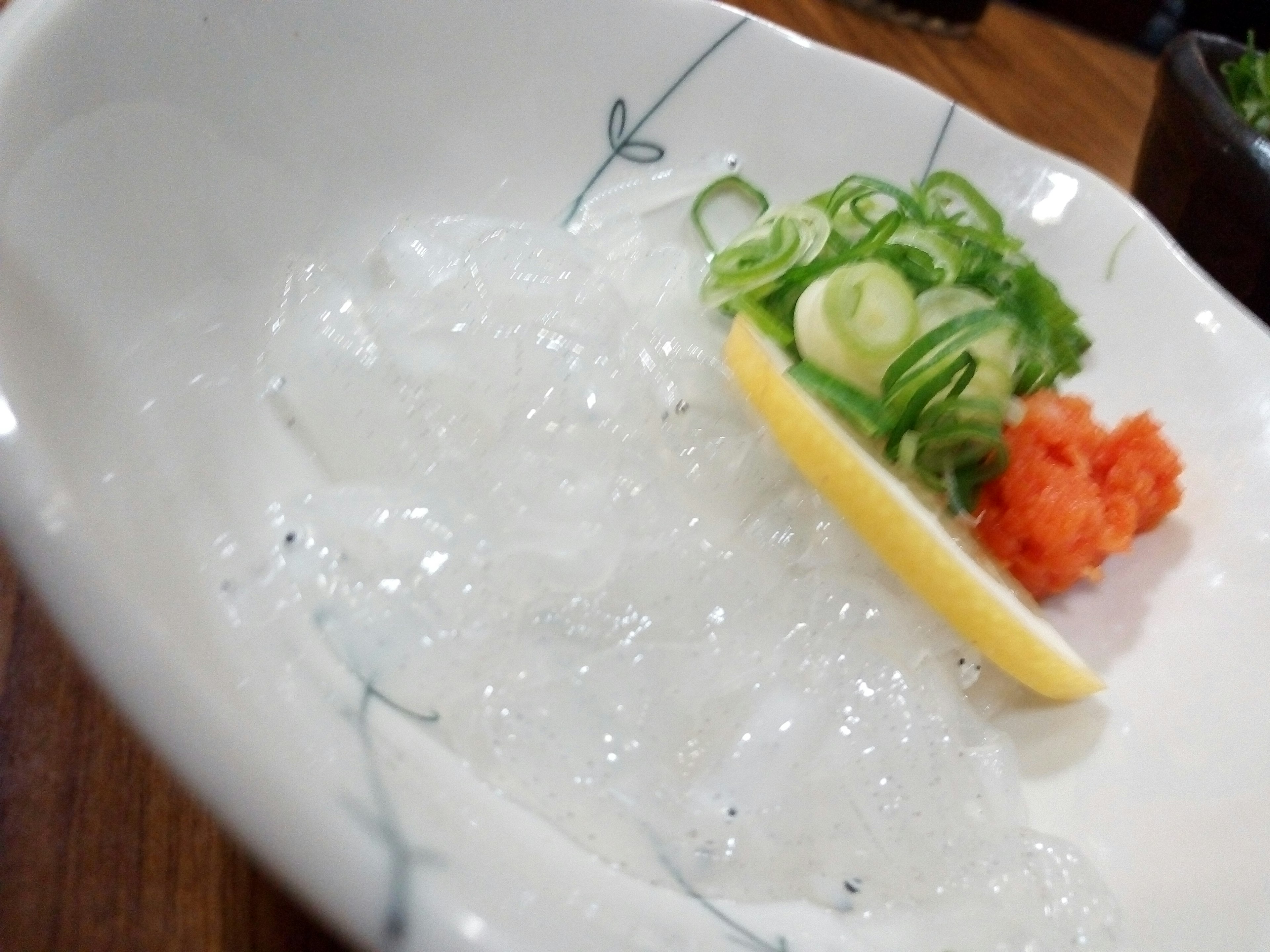 Clear sashimi with finely chopped green onions and a slice of lemon accompanied by wasabi